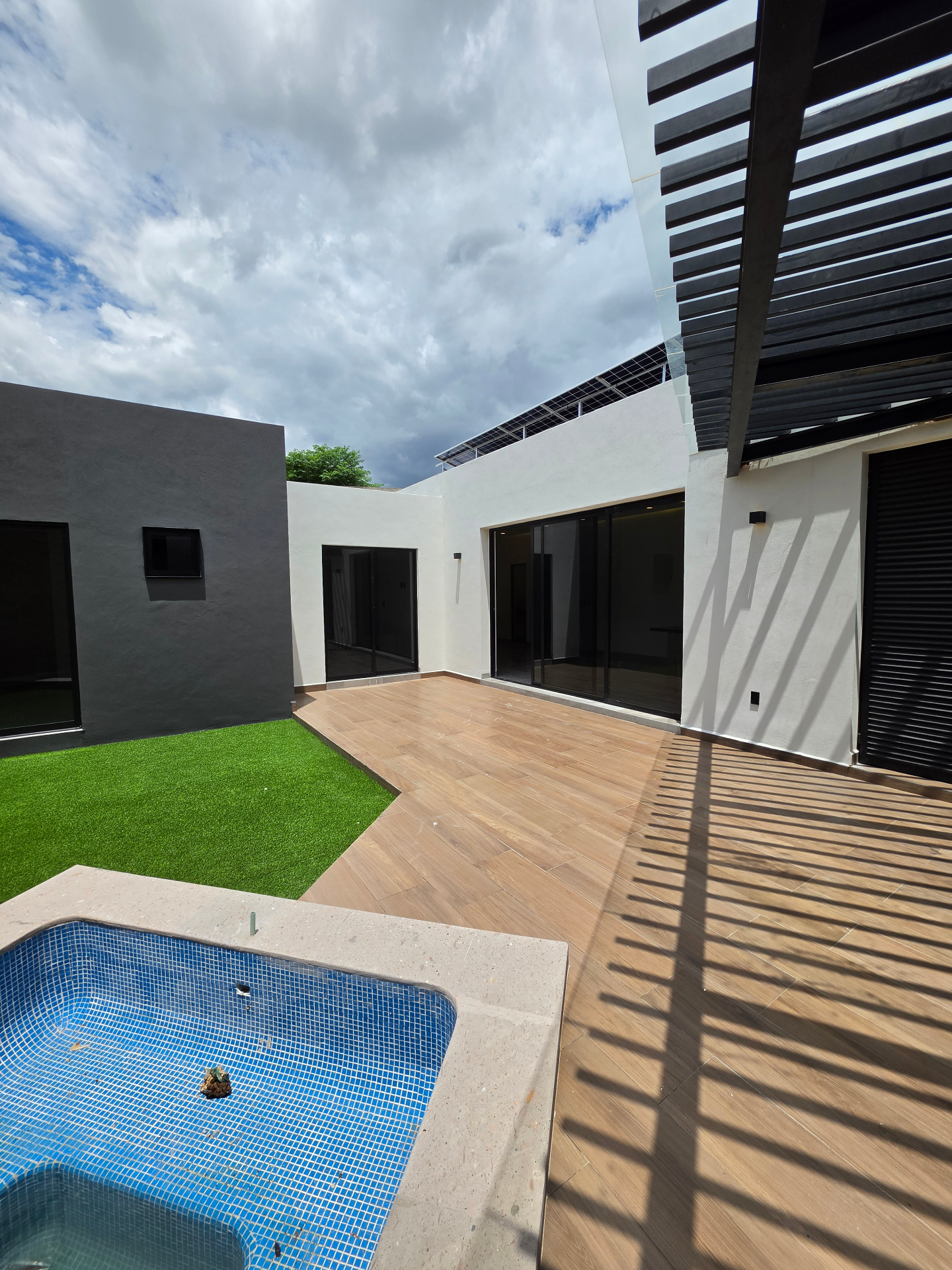 Alberca con acabado azul, deck de madera y pérgola de lamas