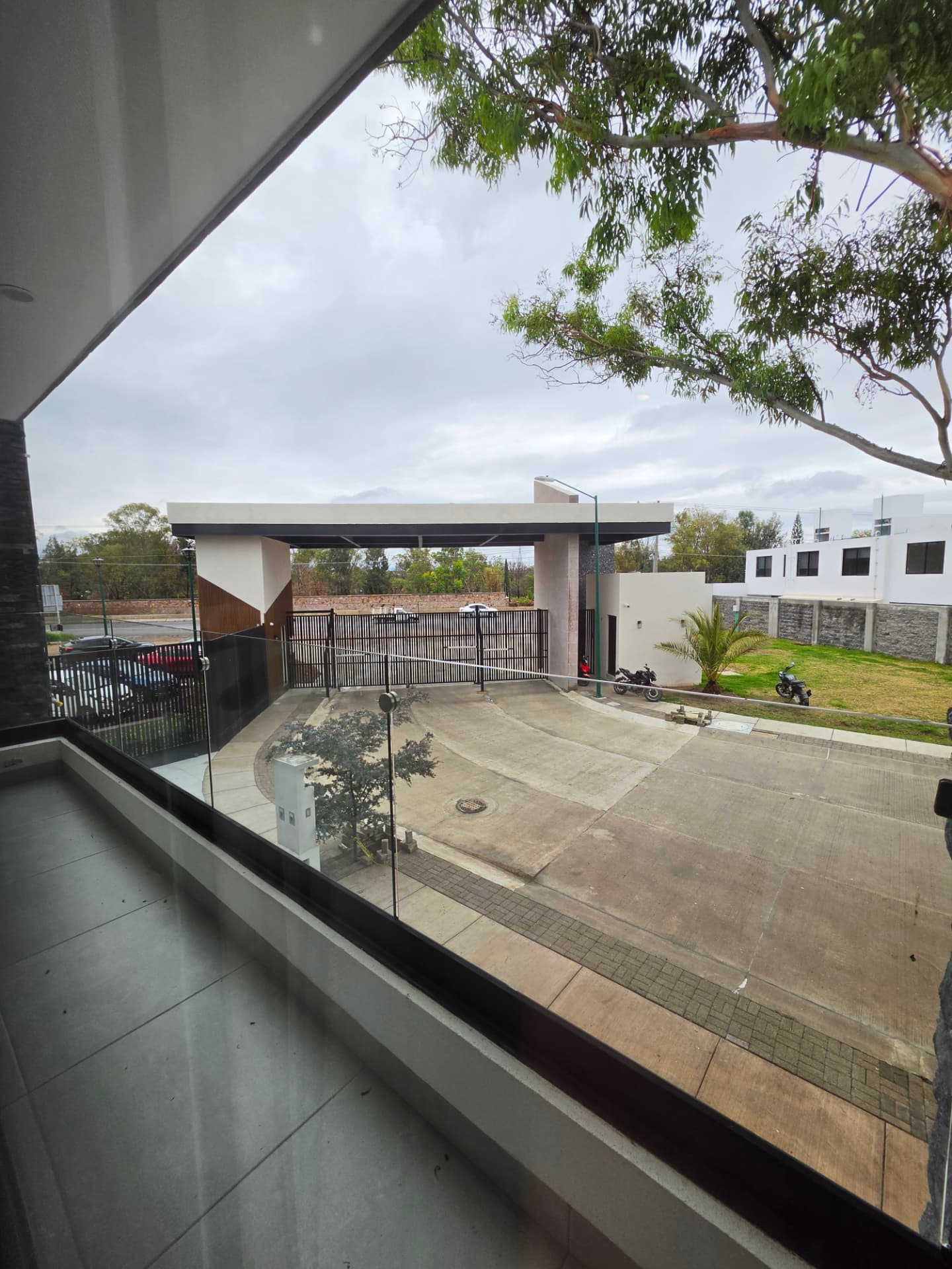 Balcón con barandal de cristal y vista al acceso principal del fraccionamiento