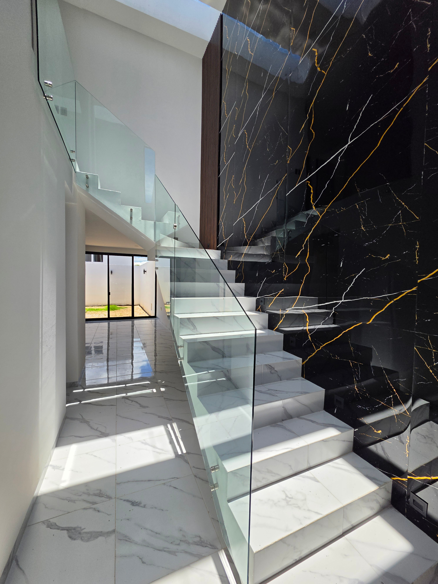 Escalera escultórica con muro de mármol negro veteado y barandal de cristal templado