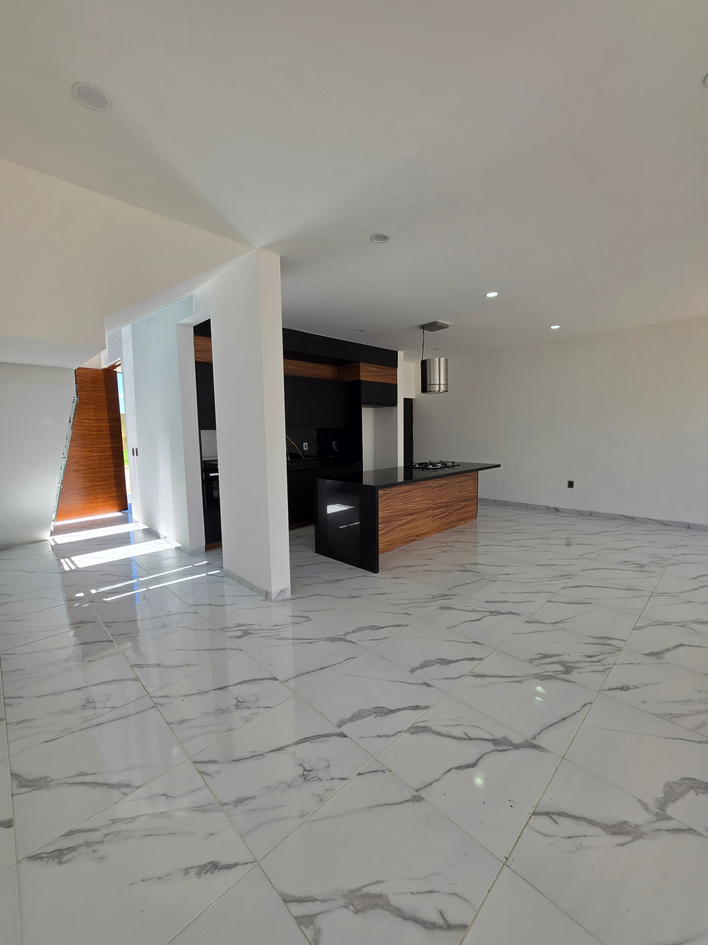 Área social amplia con piso de mármol, doble altura y vista a la cocina y escalera