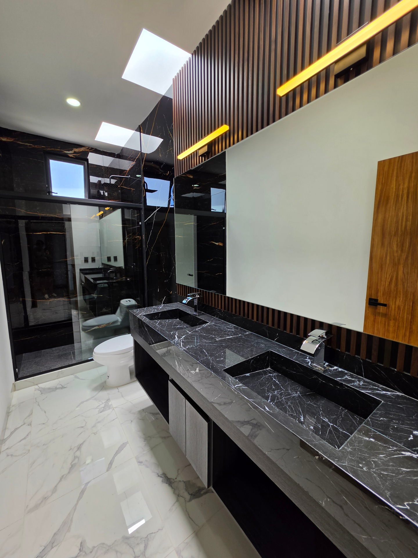 Baño principal con mármol negro, doble lavabo y detalles en madera