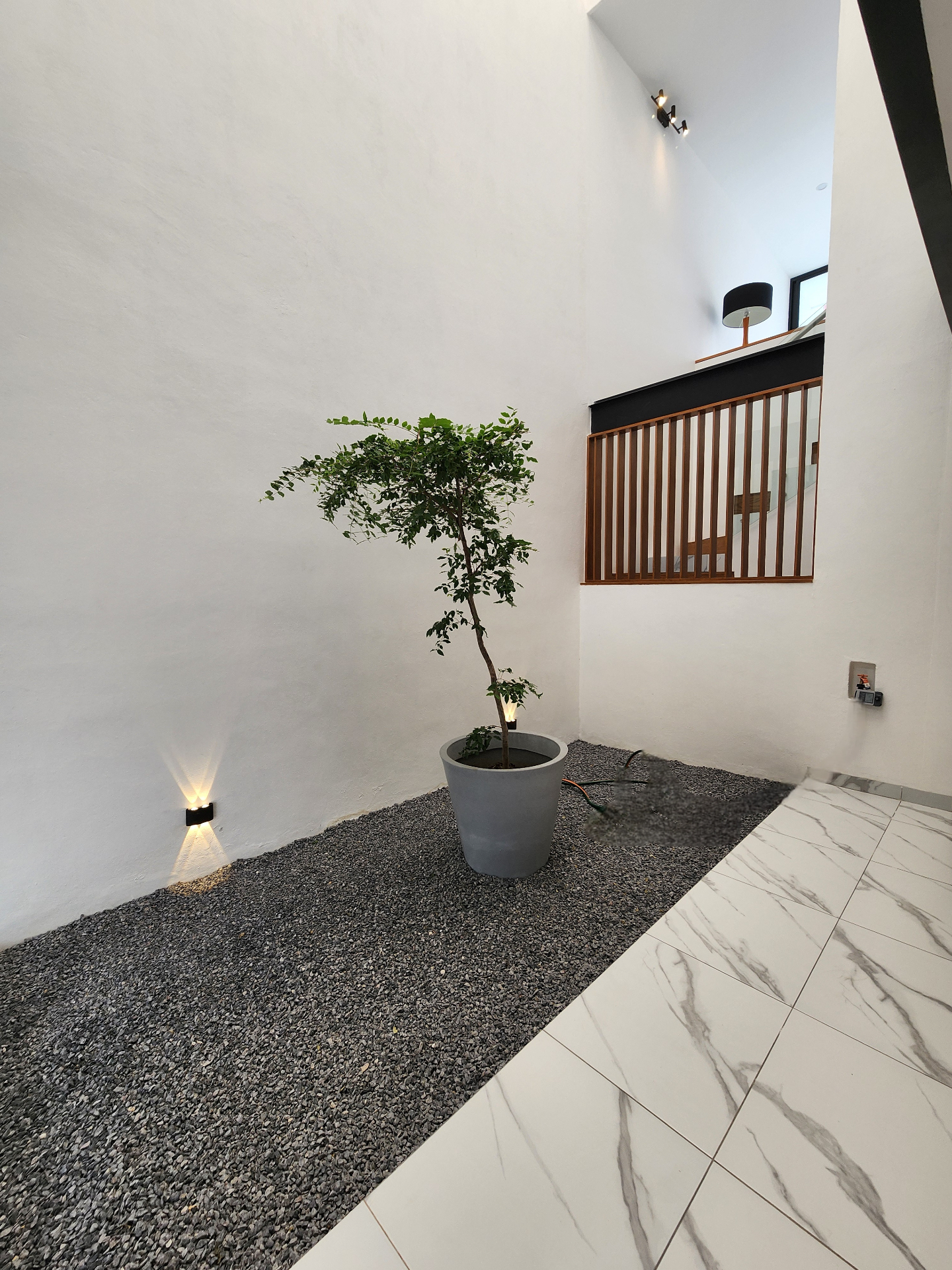 Jardín interior con doble altura, gravilla y vegetación viva