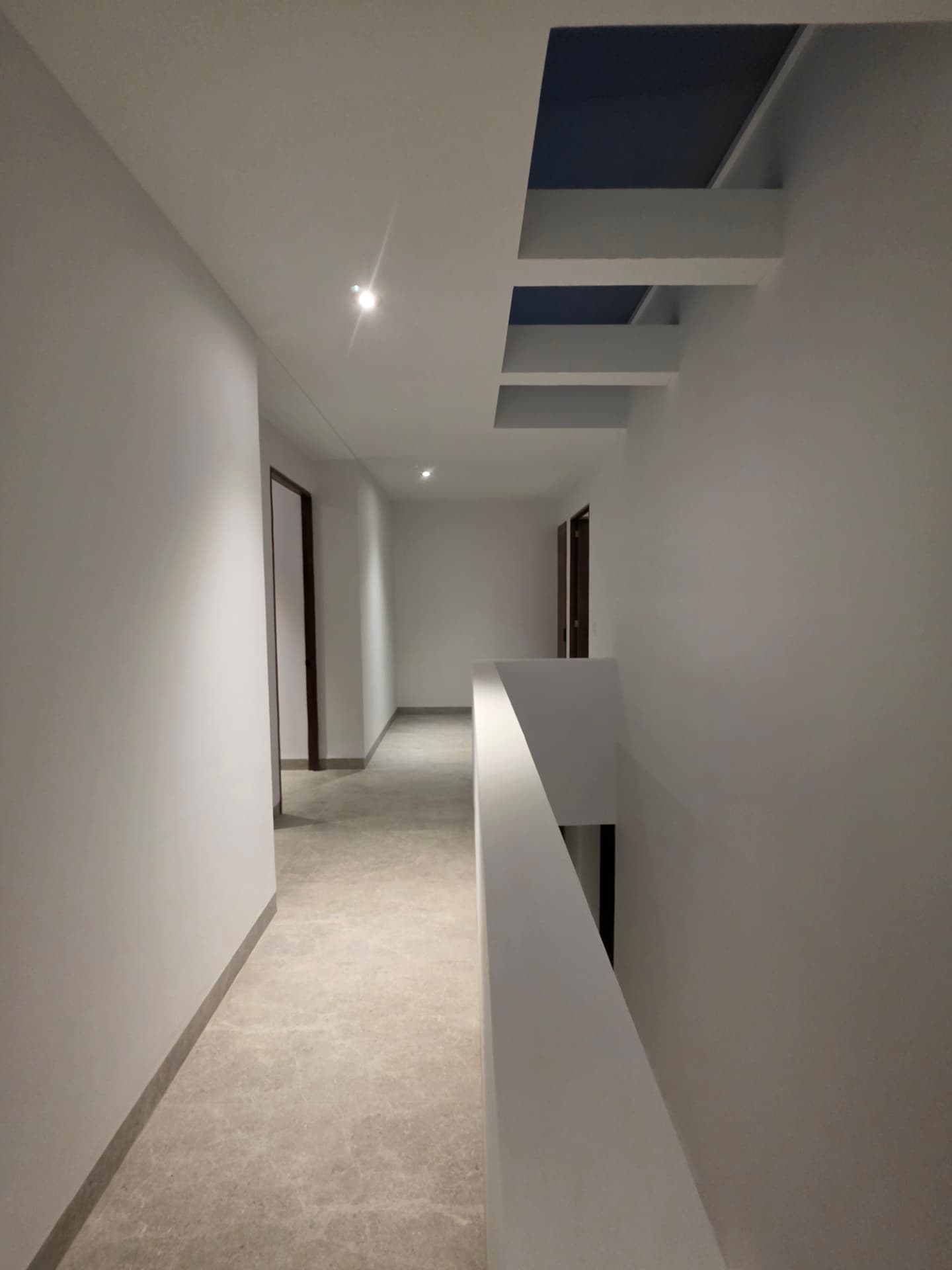 Pasillo de planta alta con doble altura, pretil blanco y vigas aparentes