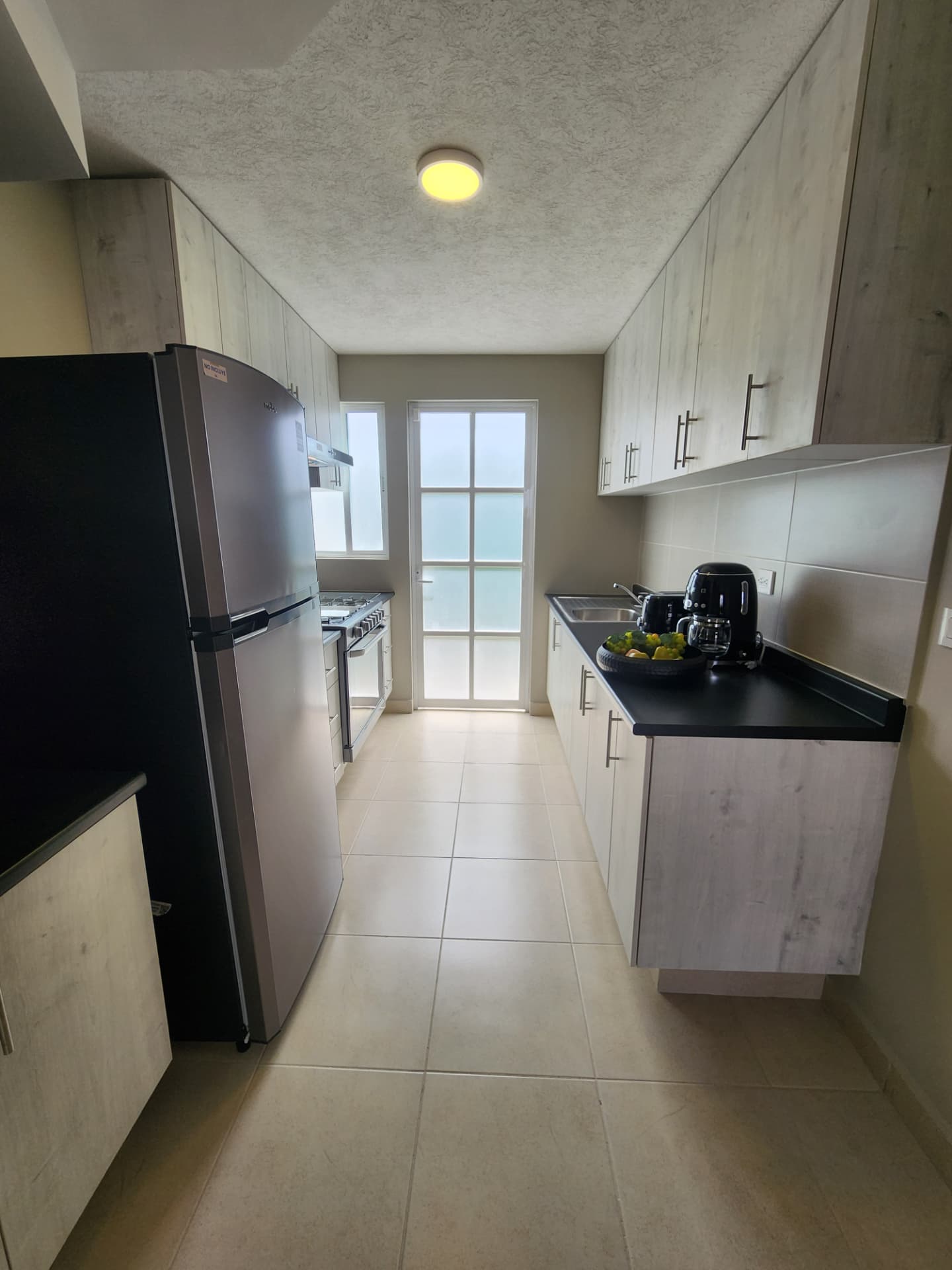 Cocina equipada con alacenas de madera, cubierta oscura y salida al patio de servicio