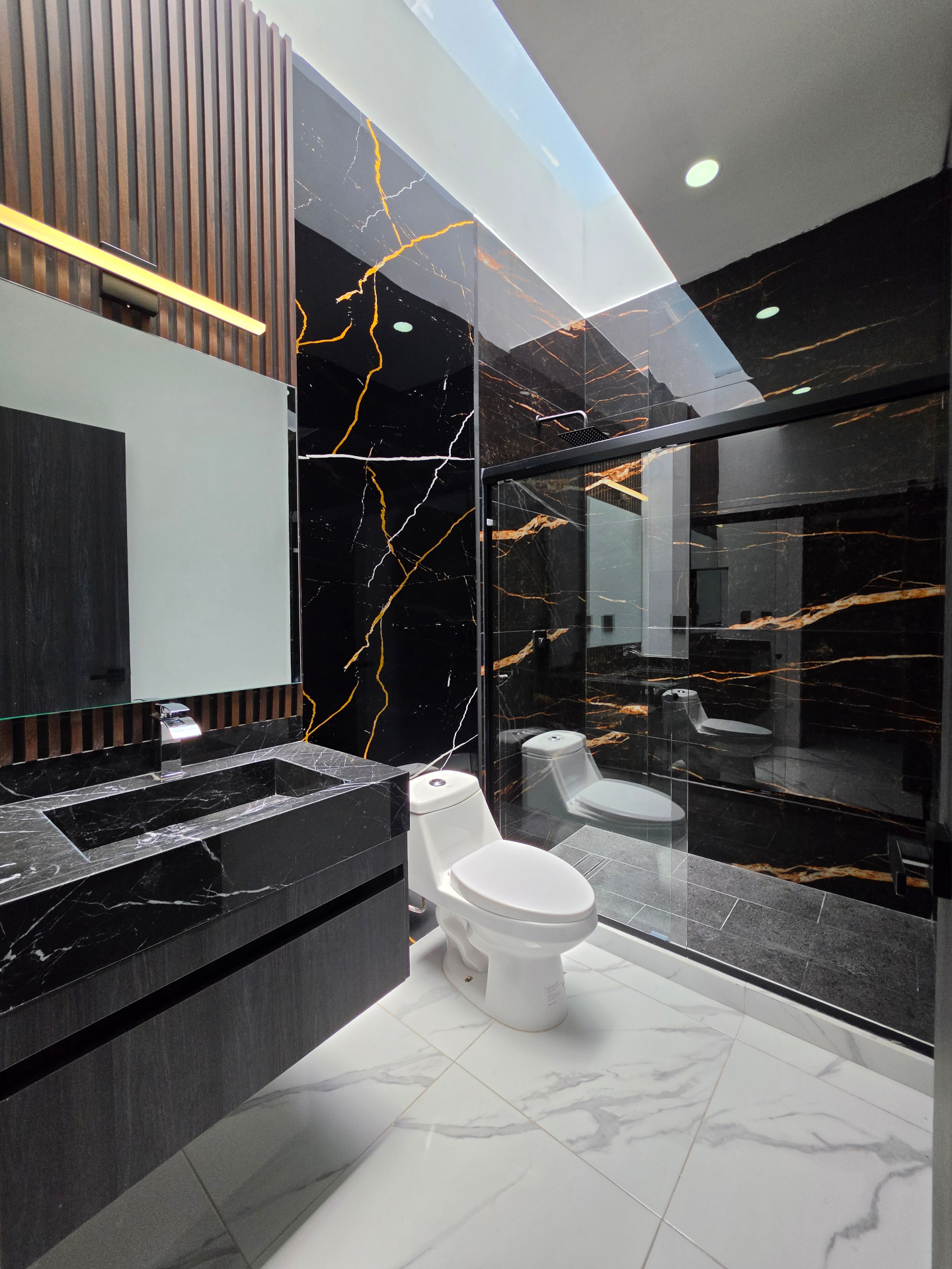 Baño completo con mármol negro veteado, cancelería de cristal y luz indirecta