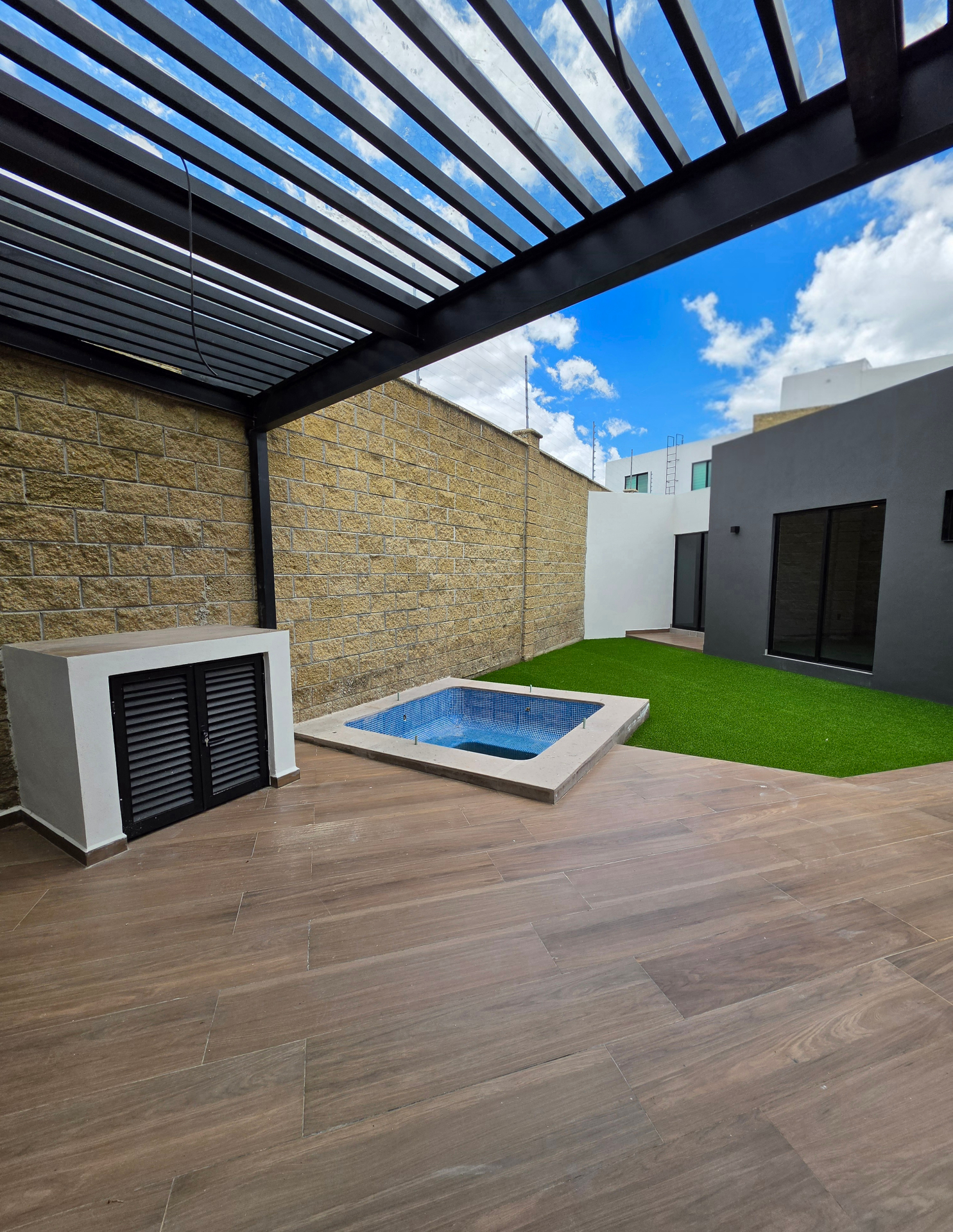 Patio trasero con pérgola metálica, chapoteadero, deck de madera y jardín