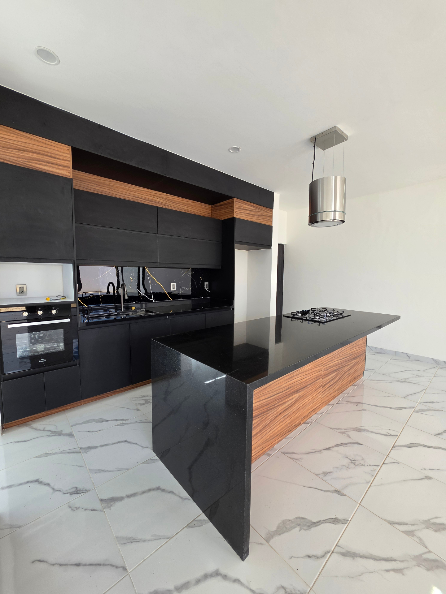 Cocina integral negra con isla forrada en madera, horno empotrado y cubierta de granito
