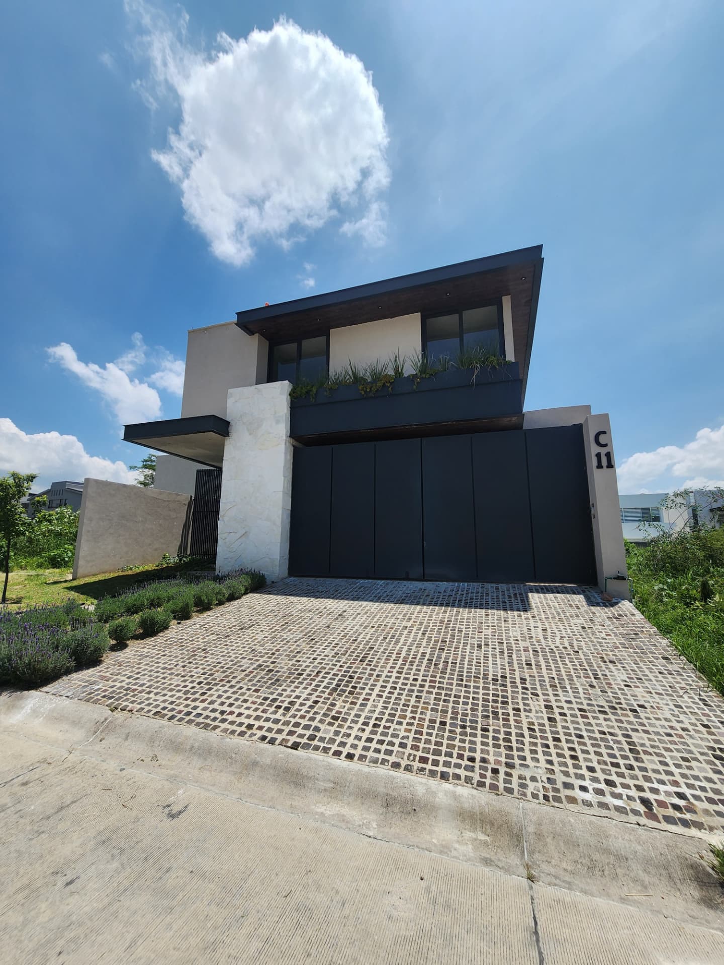 Fachada frontal con volados, muro en piedra y jardinera en balcón
