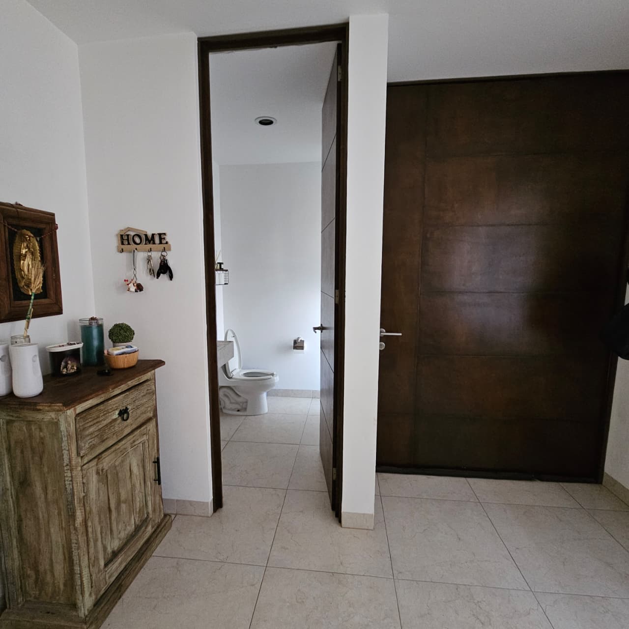 Vestíbulo de acceso con puerta principal en madera y medio baño