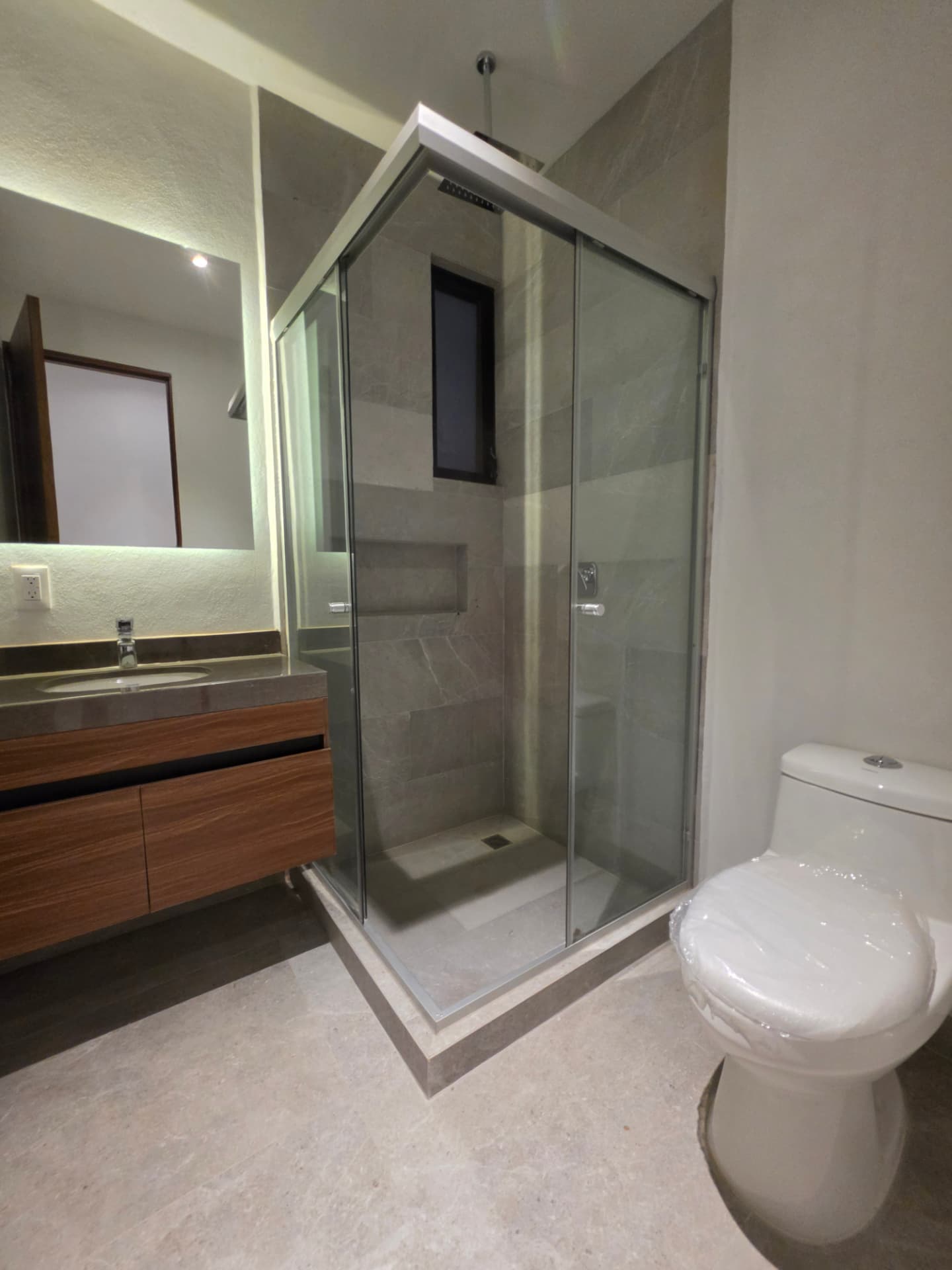 Baño con cubierta de mármol, espejo retroiluminado y regadera con cancel templado
