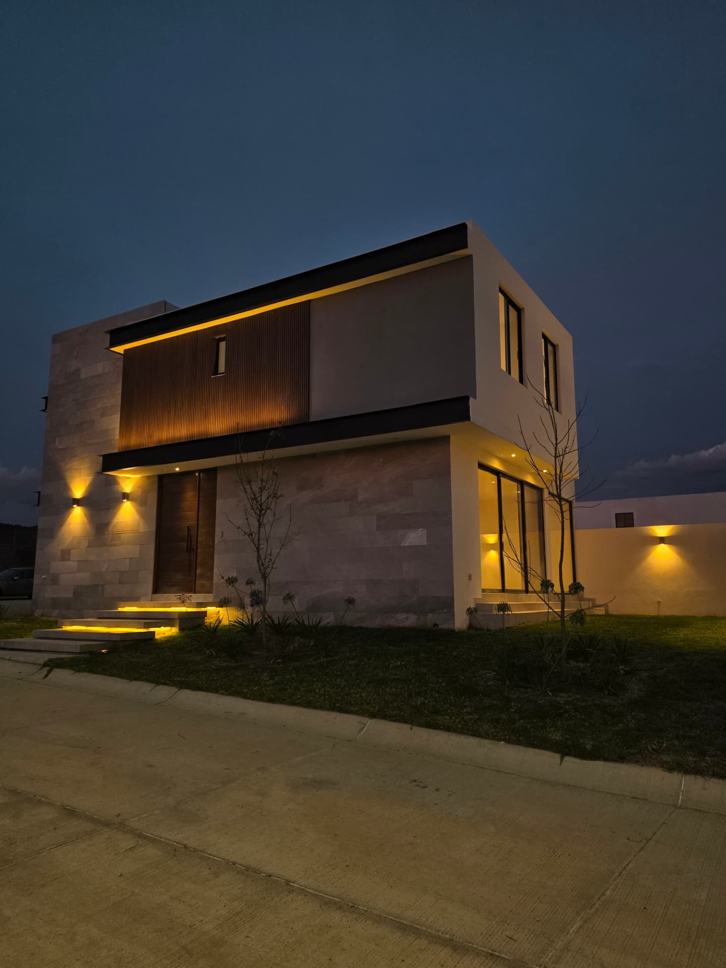 Acceso principal iluminado con puerta de madera, celosía y escalinatas con luz integrada