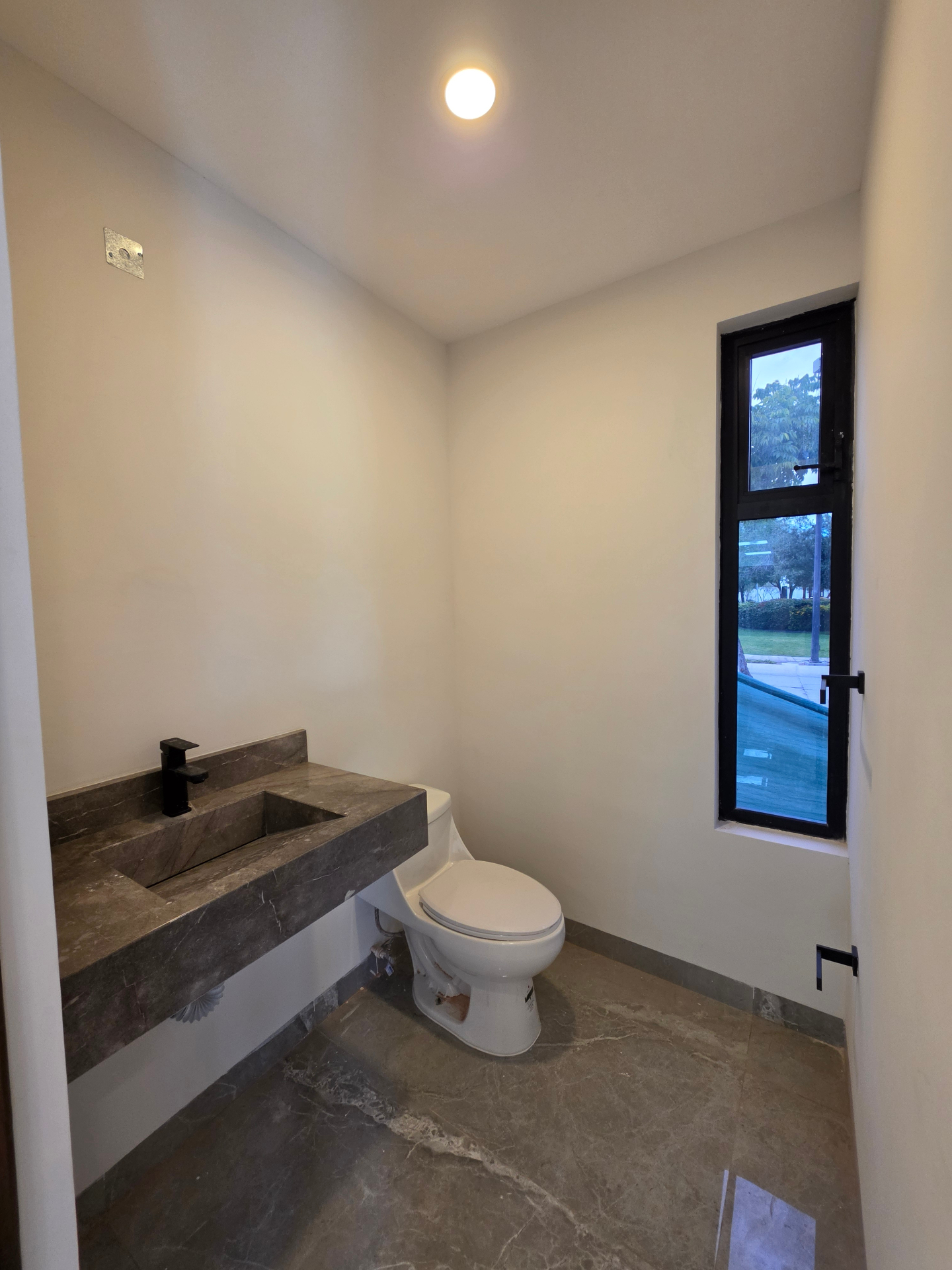 Medio baño con lavabo de mármol, grifería negra y ventanal vertical