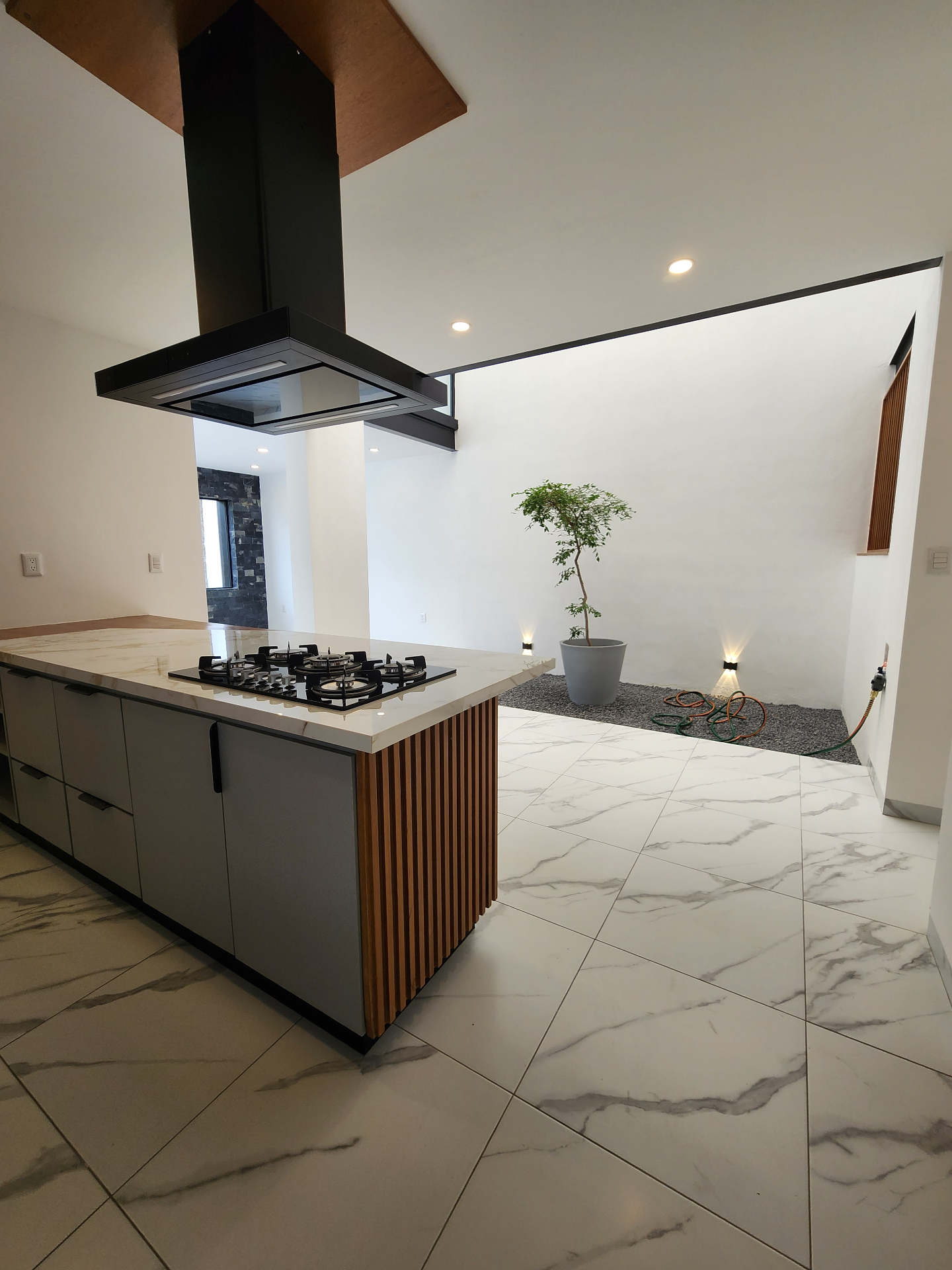 Cocina abierta al jardín interior con isla de mármol y parrilla de gas