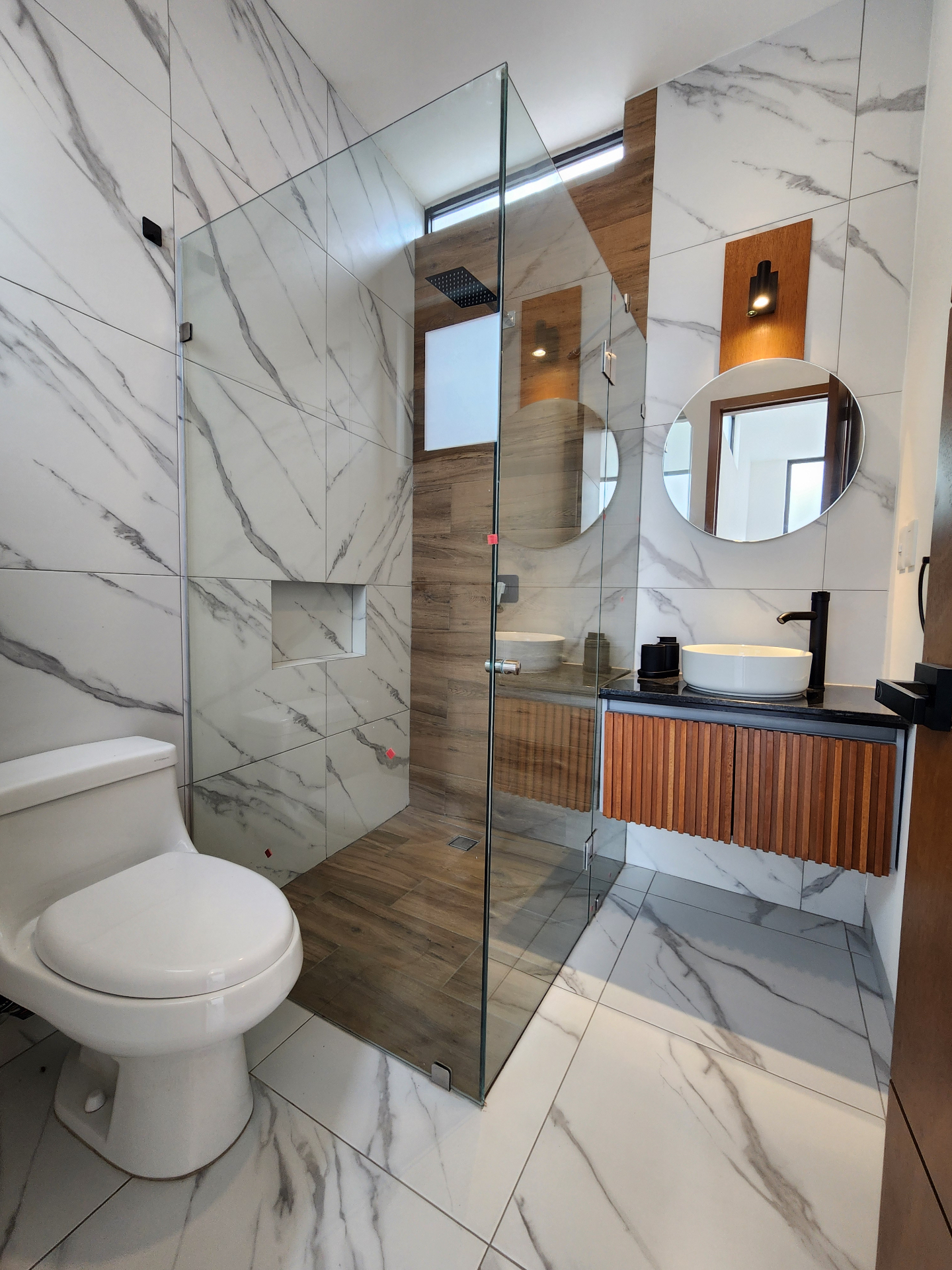 Baño con cancel de cristal templado, regadera tipo lluvia y mueble de madera