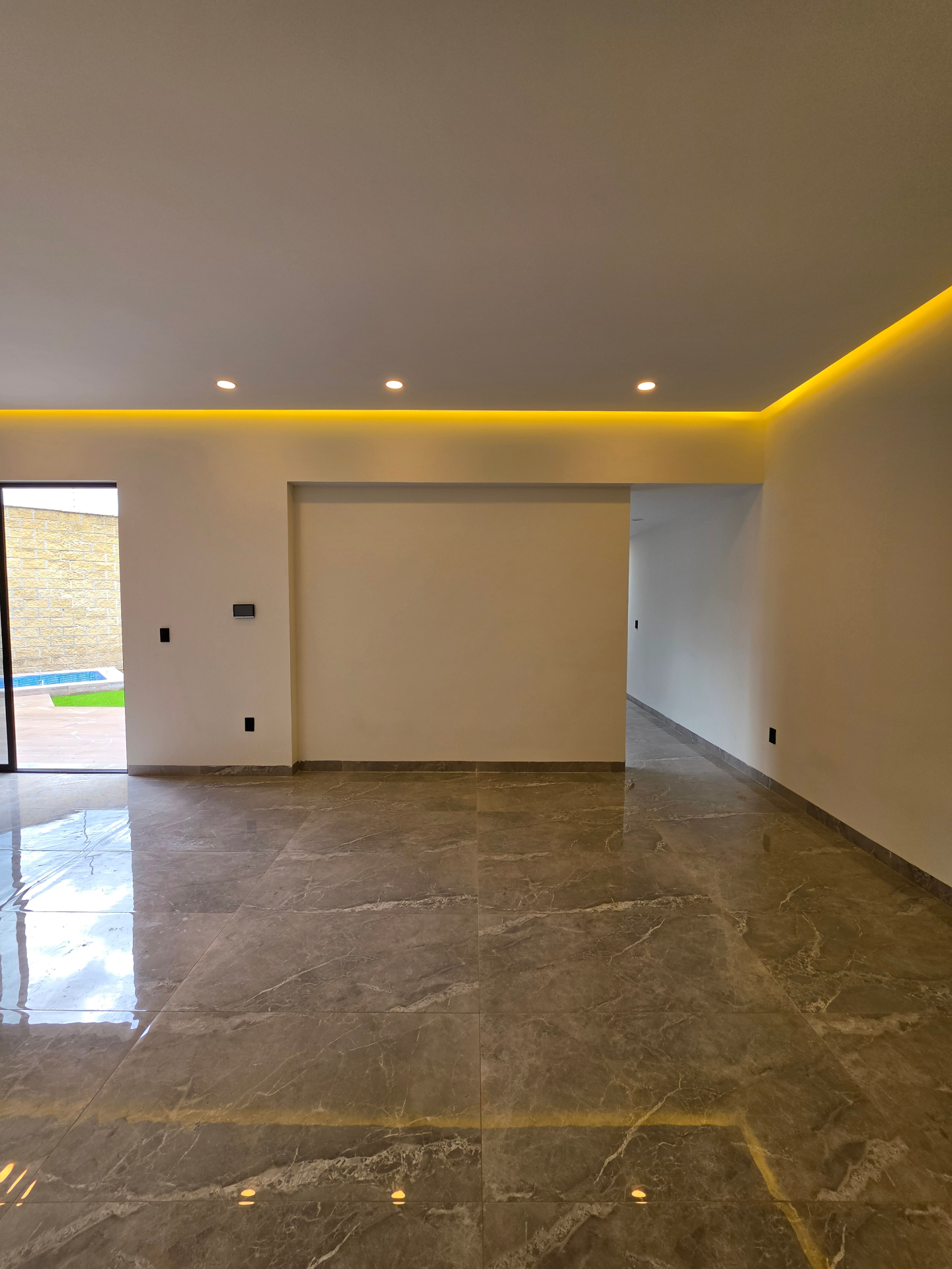 Sala amplia con piso de mármol pulido, iluminación LED indirecta y acceso a alberca