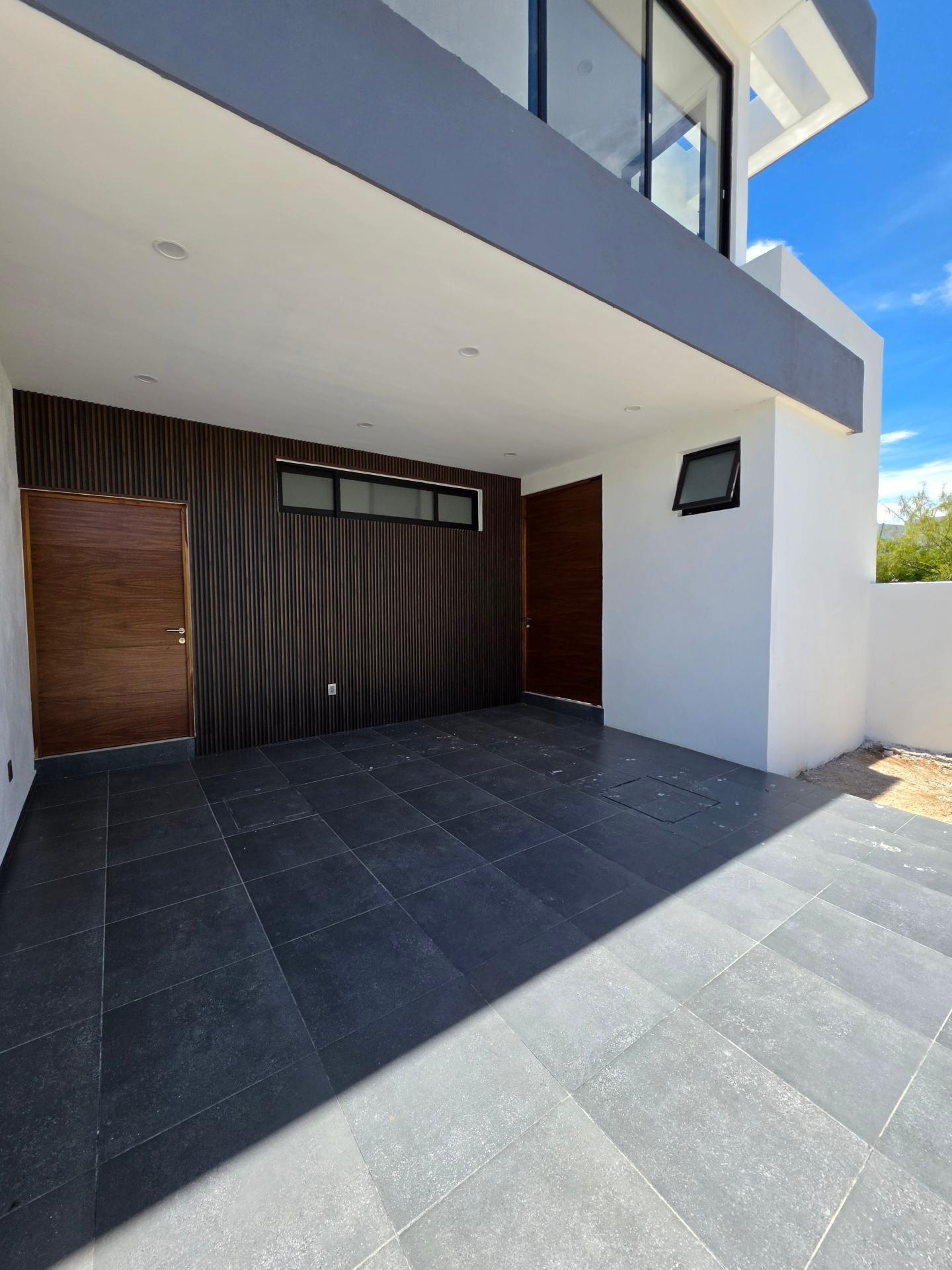 Cochera techada con muro de listones de madera y piso porcelánico negro
