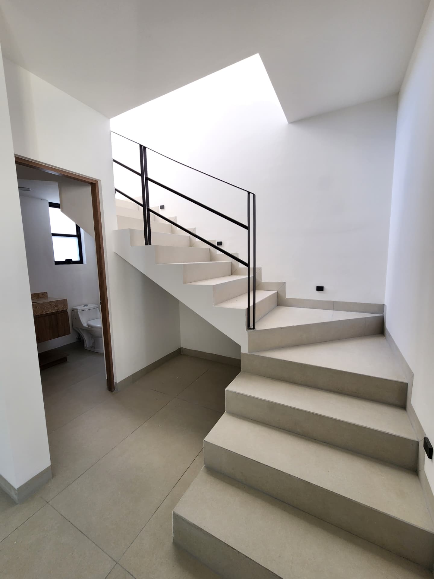 Escalera con barandal metálico, tragaluz y acceso a medio baño