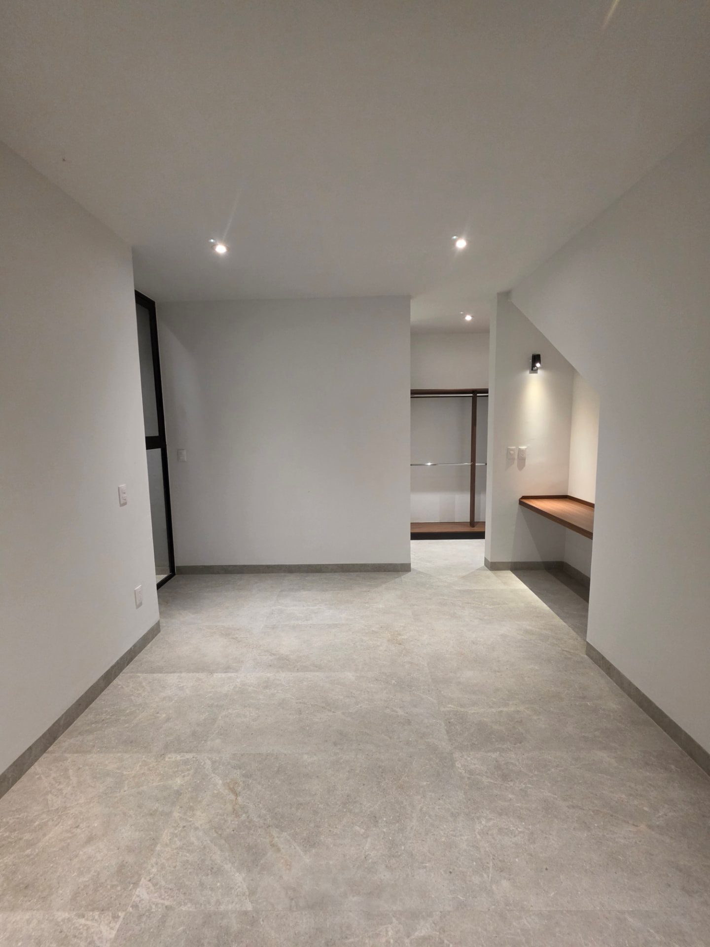 Recámara amplia con vestidor integrado, escritorio de madera y piso porcelánico gris