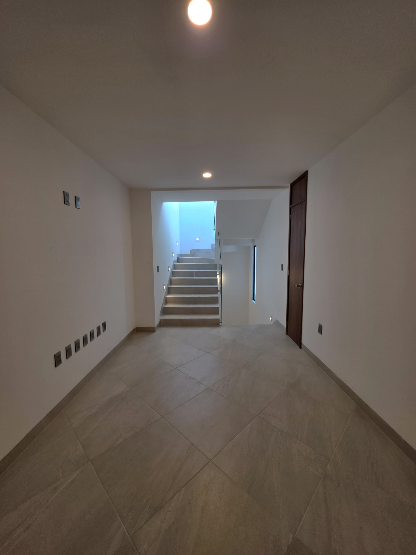 Vestíbulo con escalera iluminada y barandal de cristal templado