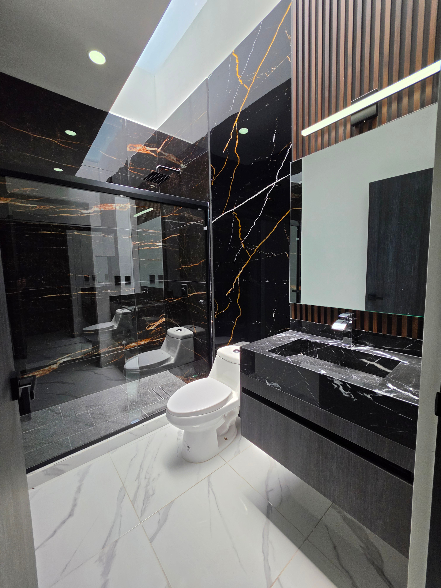 Vista frontal del baño con lavabo escultórico, espejo flotante y regadera amplia
