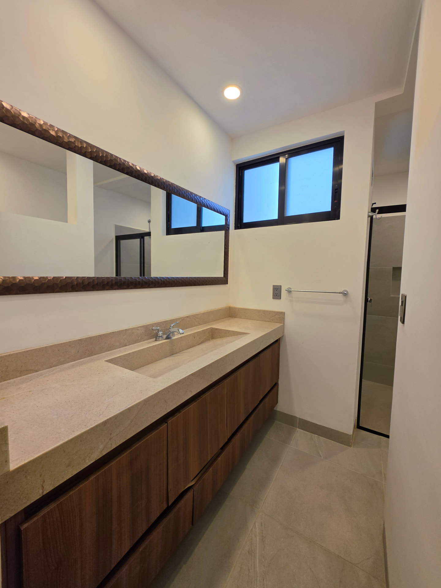 Baño con cubierta de piedra, mueble de madera y regadera con cancel