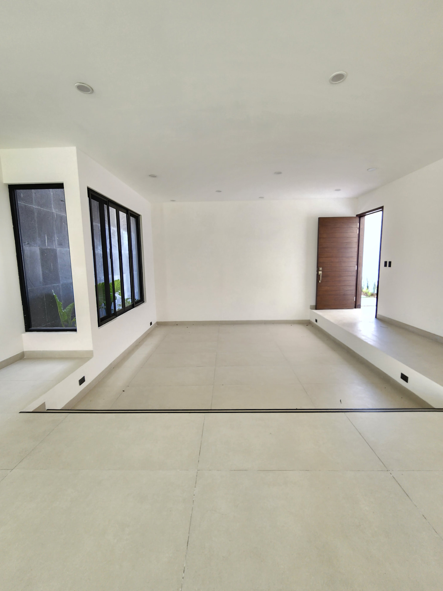 Estancia amplia con acceso principal de madera y ventanales al jardín interior