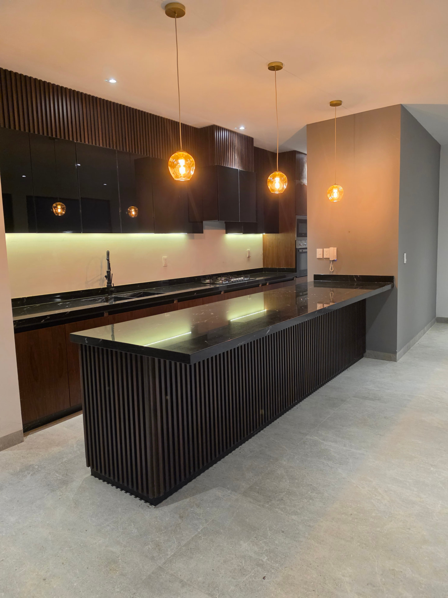 Cocina equipada con carpintería oscura, cubierta de mármol negro, barra desayunador e iluminación LED