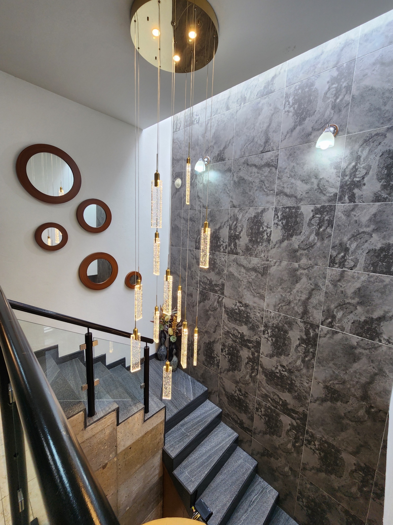 Escalera de doble altura con muro cerámico y luminarias colgantes decorativas