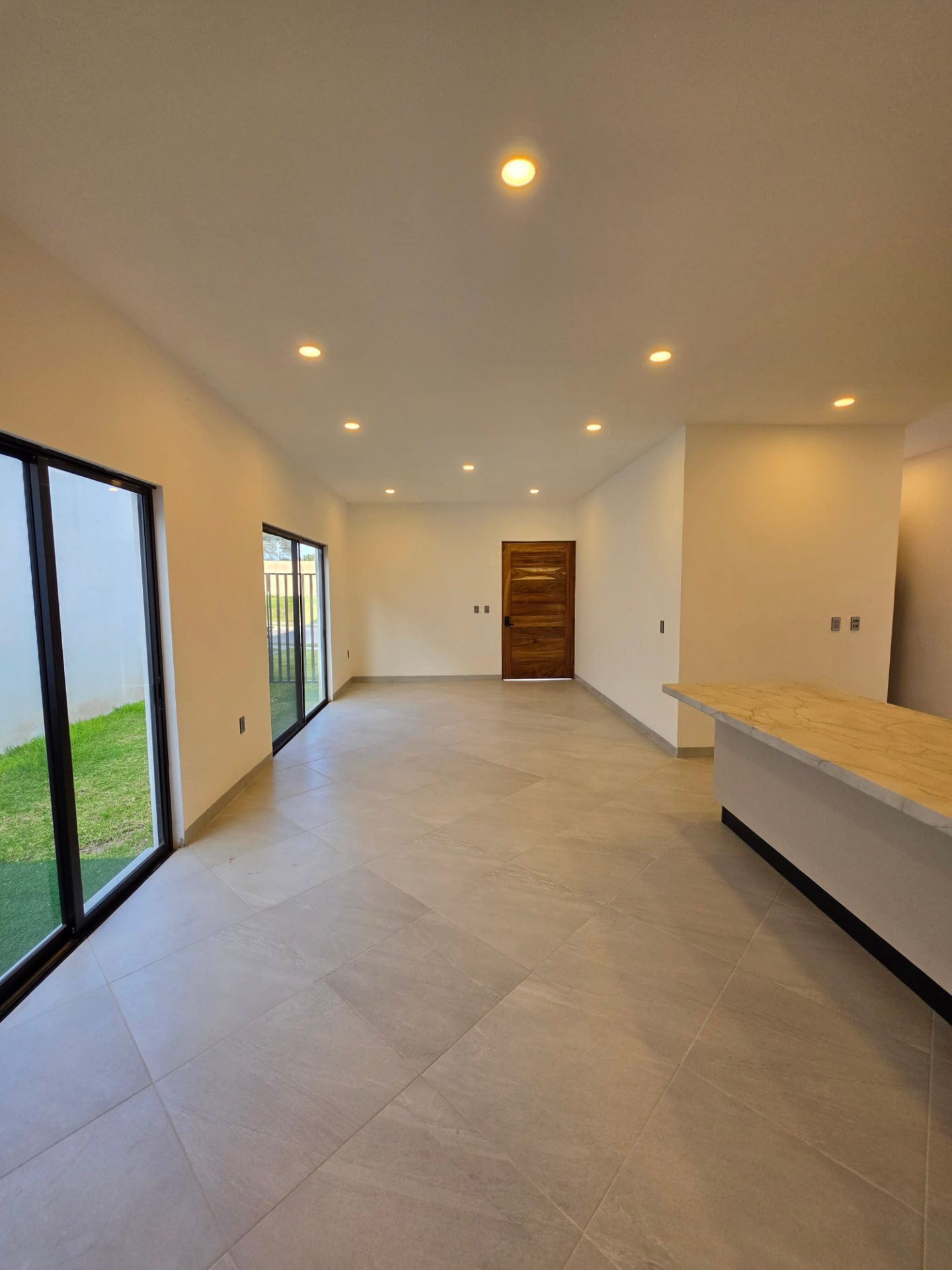 Sala y comedor con ventanales corredizos de piso a techo y jardín