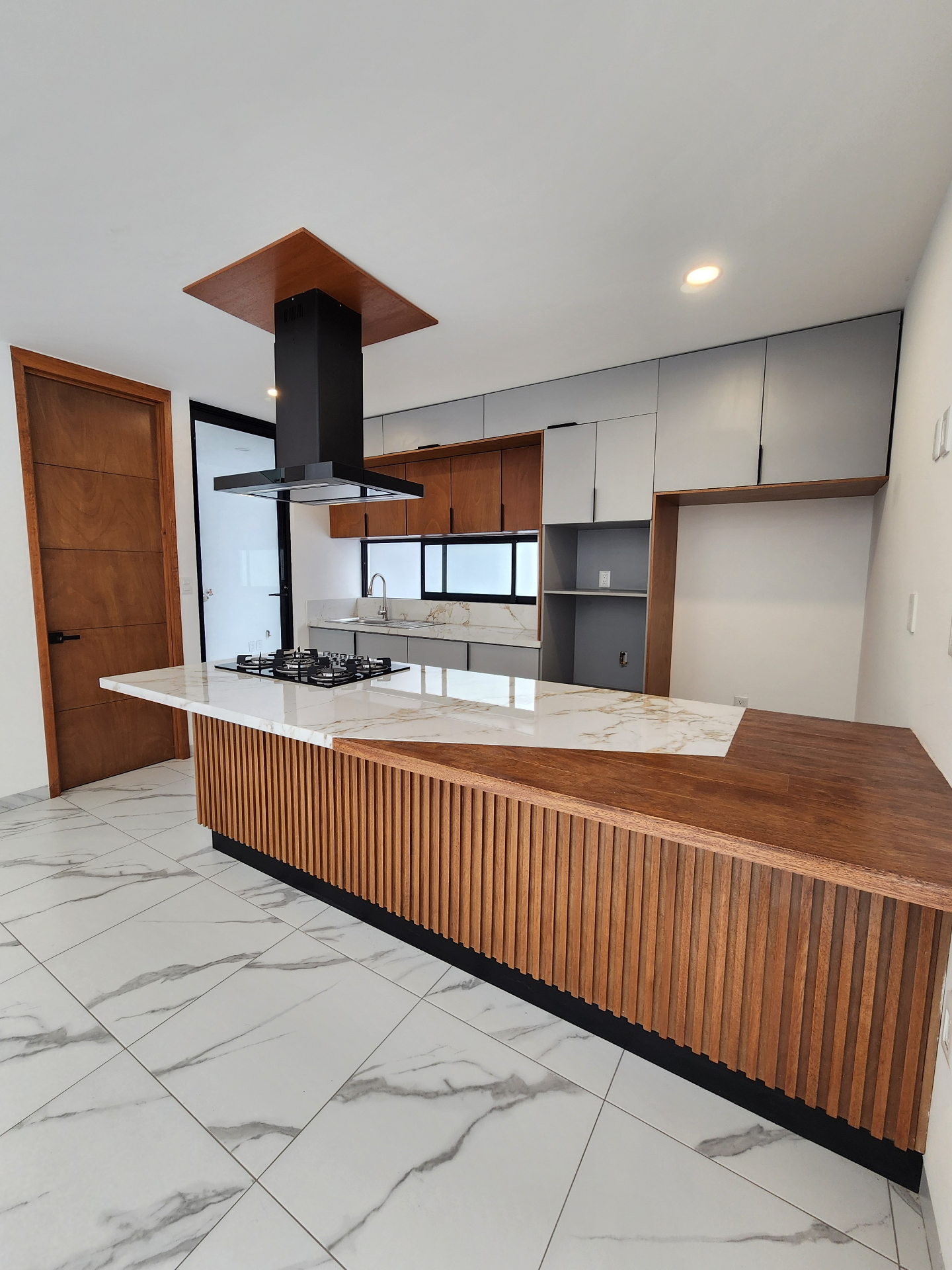 Cocina con isla central de mármol, alacenas en madera y campana negra