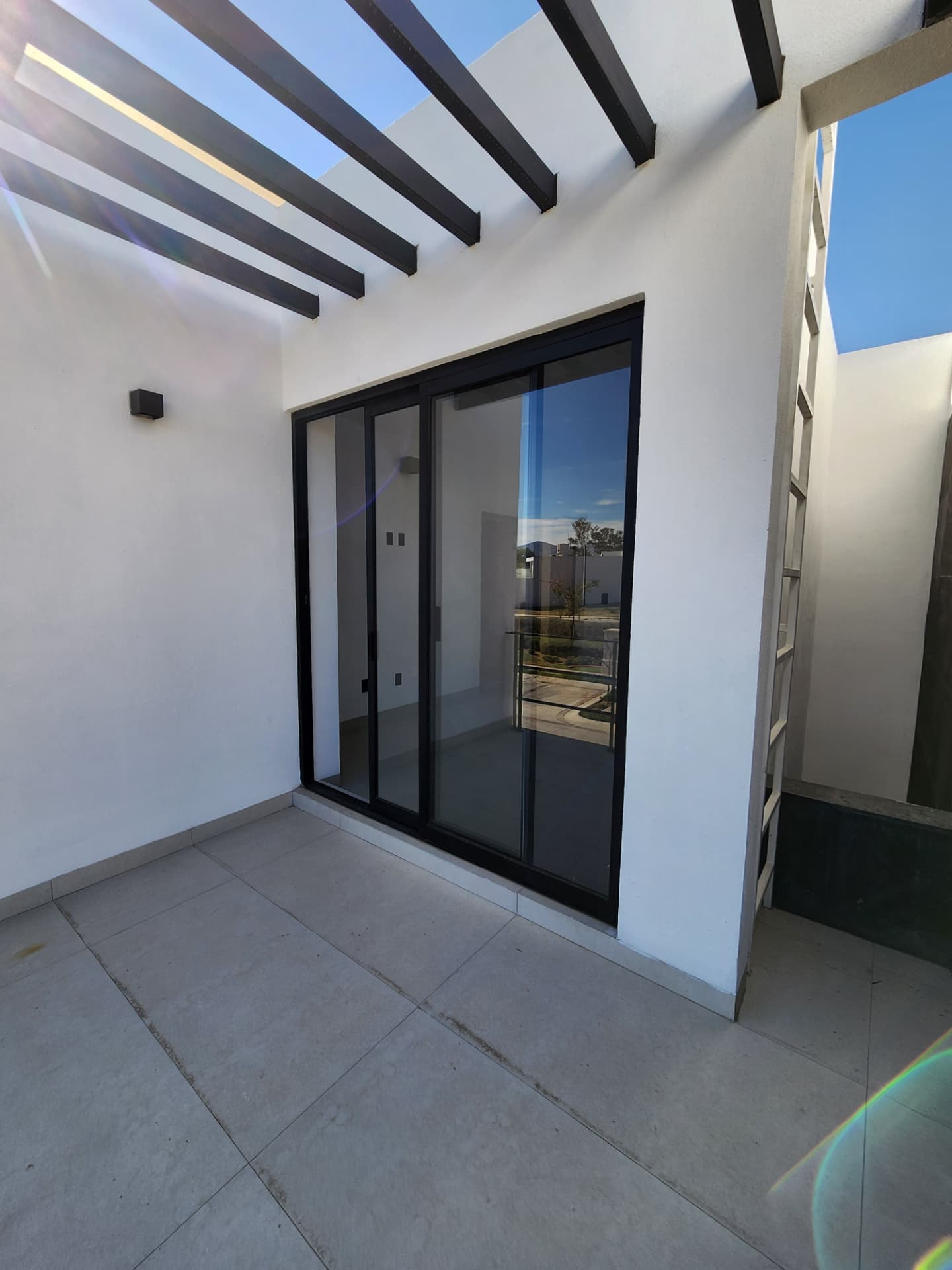 Terraza con pérgola metálica y ventanal corredizo