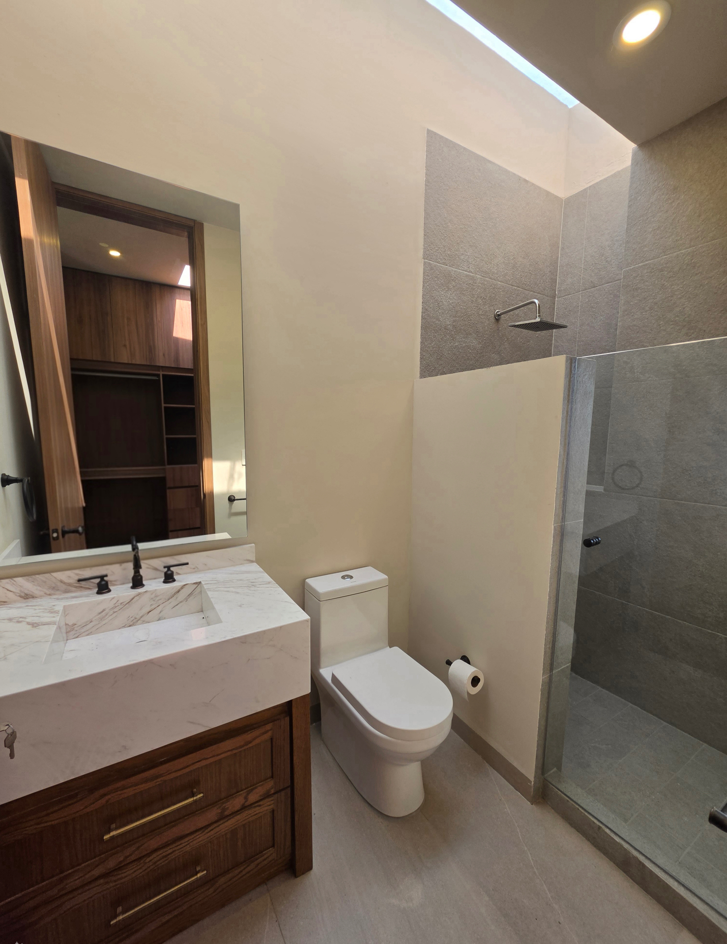 Baño en mármol con regadera de cristal y vestidor en madera