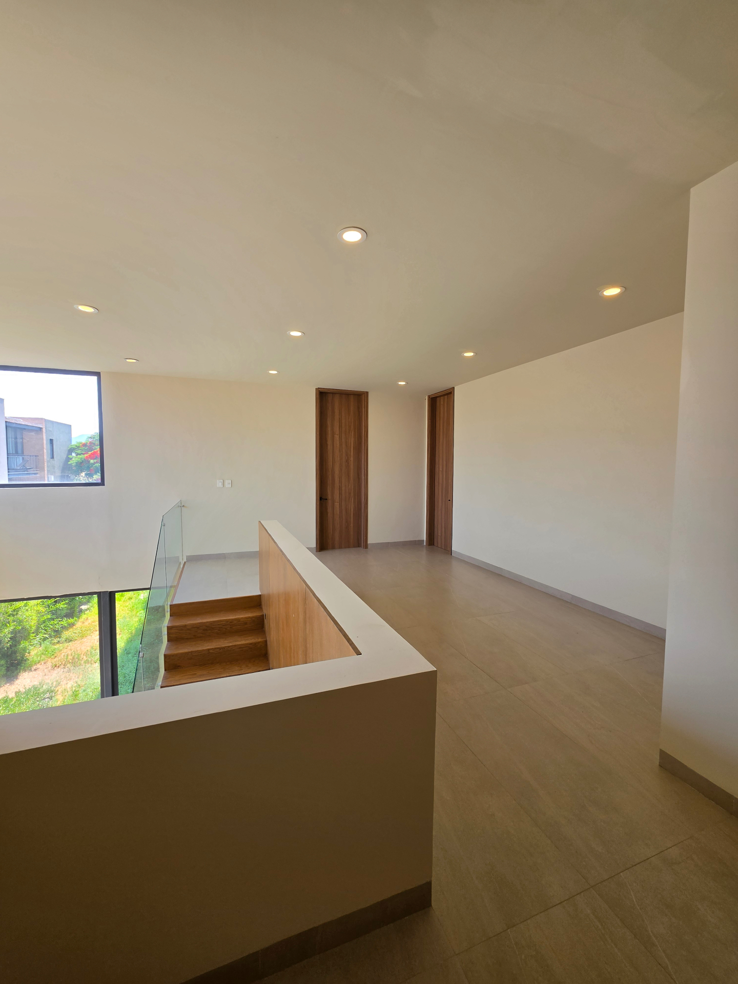 Sala de TV en planta alta con escalera de madera y barandal en cristal