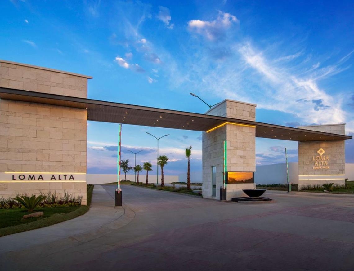 Acceso residencial Loma Alta Loreta con caseta de vigilancia y pórtico de cantera iluminado