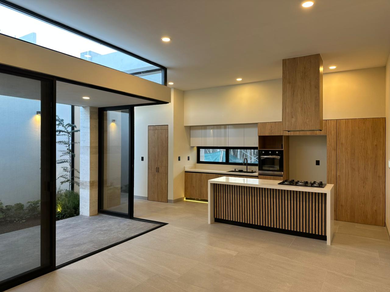 Cocina equipada con isla, campana de madera, parrilla a gas y acceso a jardín interior