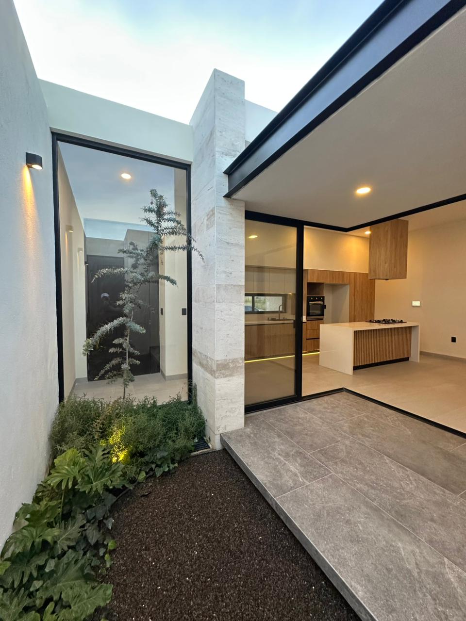 Jardín interior con muro de travertino, vegetación y conexión visual con cocina