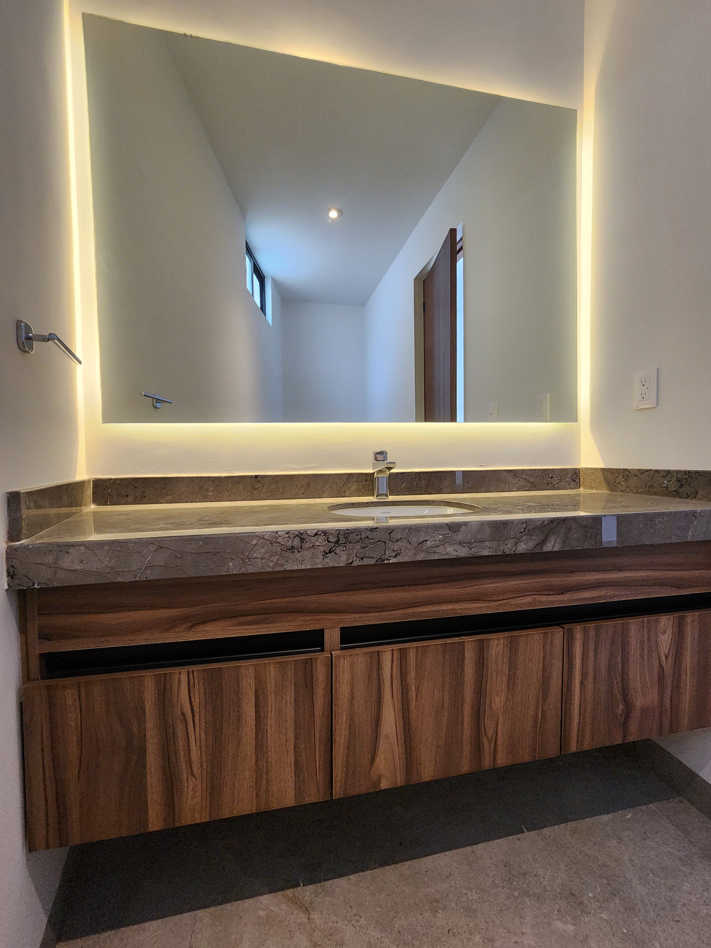 Baño principal con cubierta en mármol, lavabo bajo encimera y espejo retroiluminado