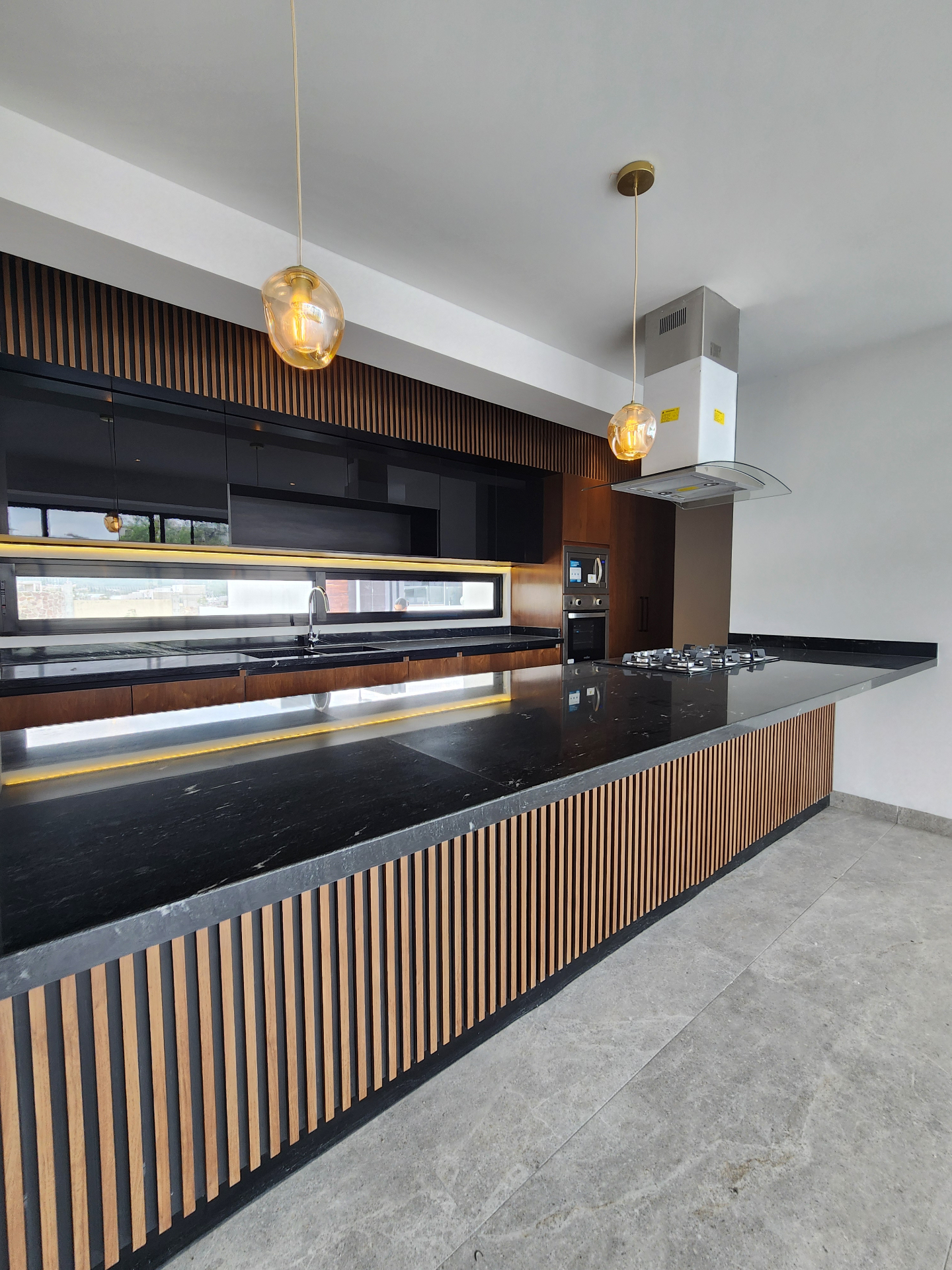Cocina con isla en granito negro, parrilla de gas y detalles en madera
