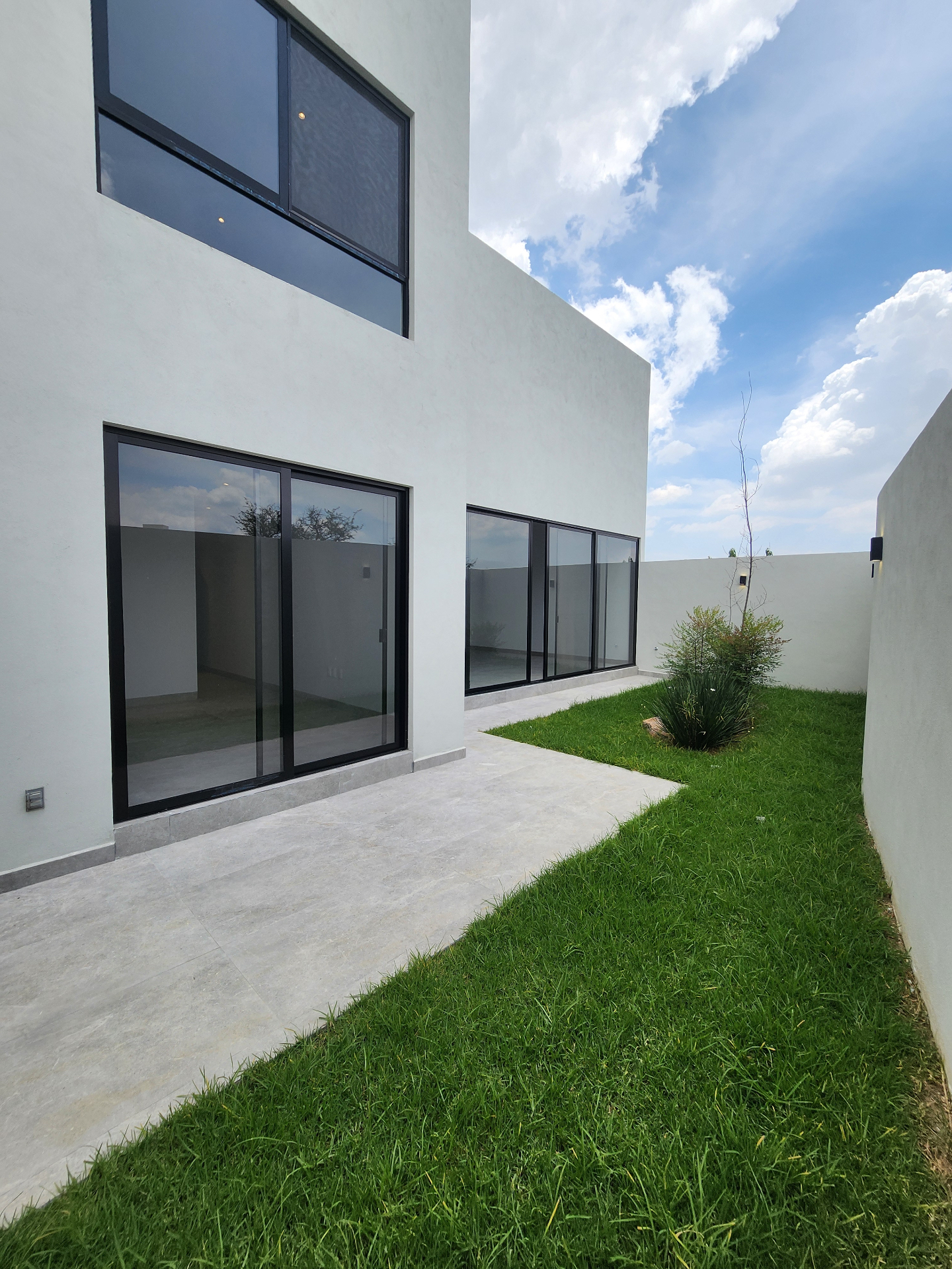 Jardín trasero con pasillo lateral y ventanales corredizos a sala y comedor
