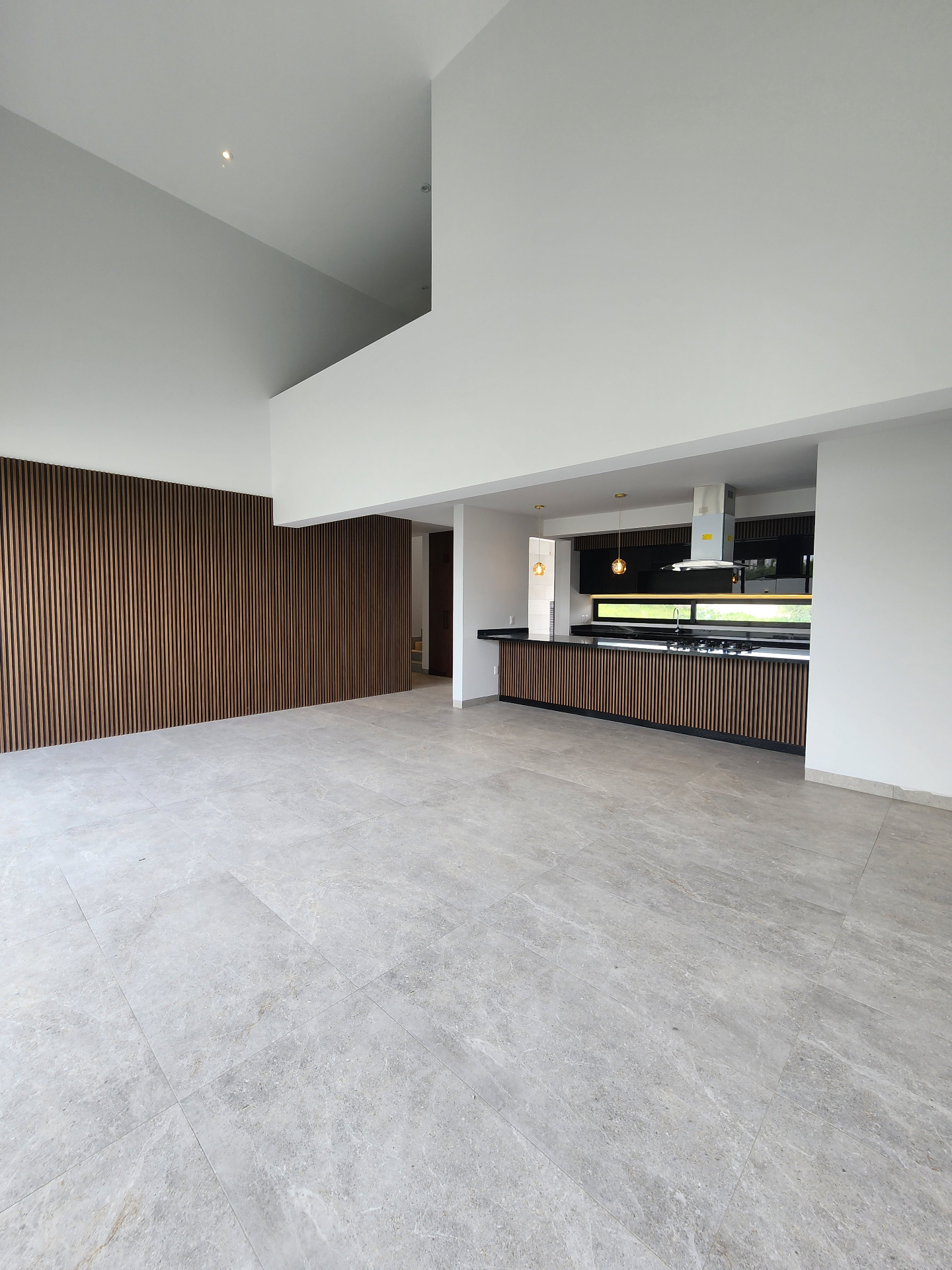 Área social de doble altura con vista abierta hacia la cocina integral y muros en acabado listonado