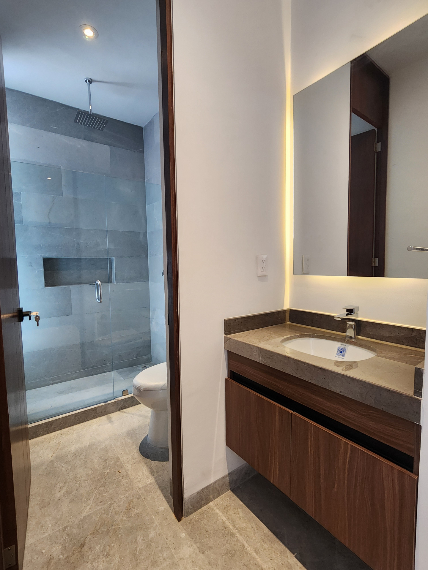 Baño con cubierta de mármol, espejo retroiluminado y regadera con cancel templado y nicho integrado
