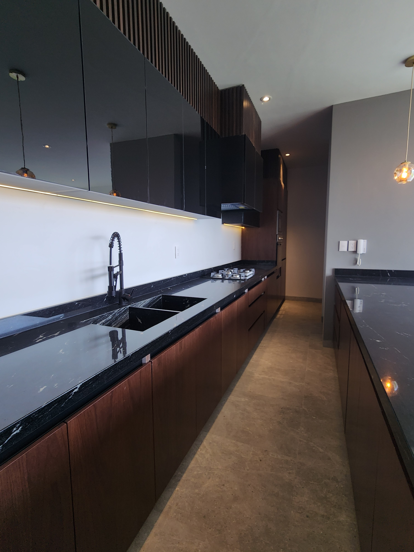 Cocina integral lineal con carpintería en nogal, cubierta de granito negro y alacenas en laca oscura con iluminación LED