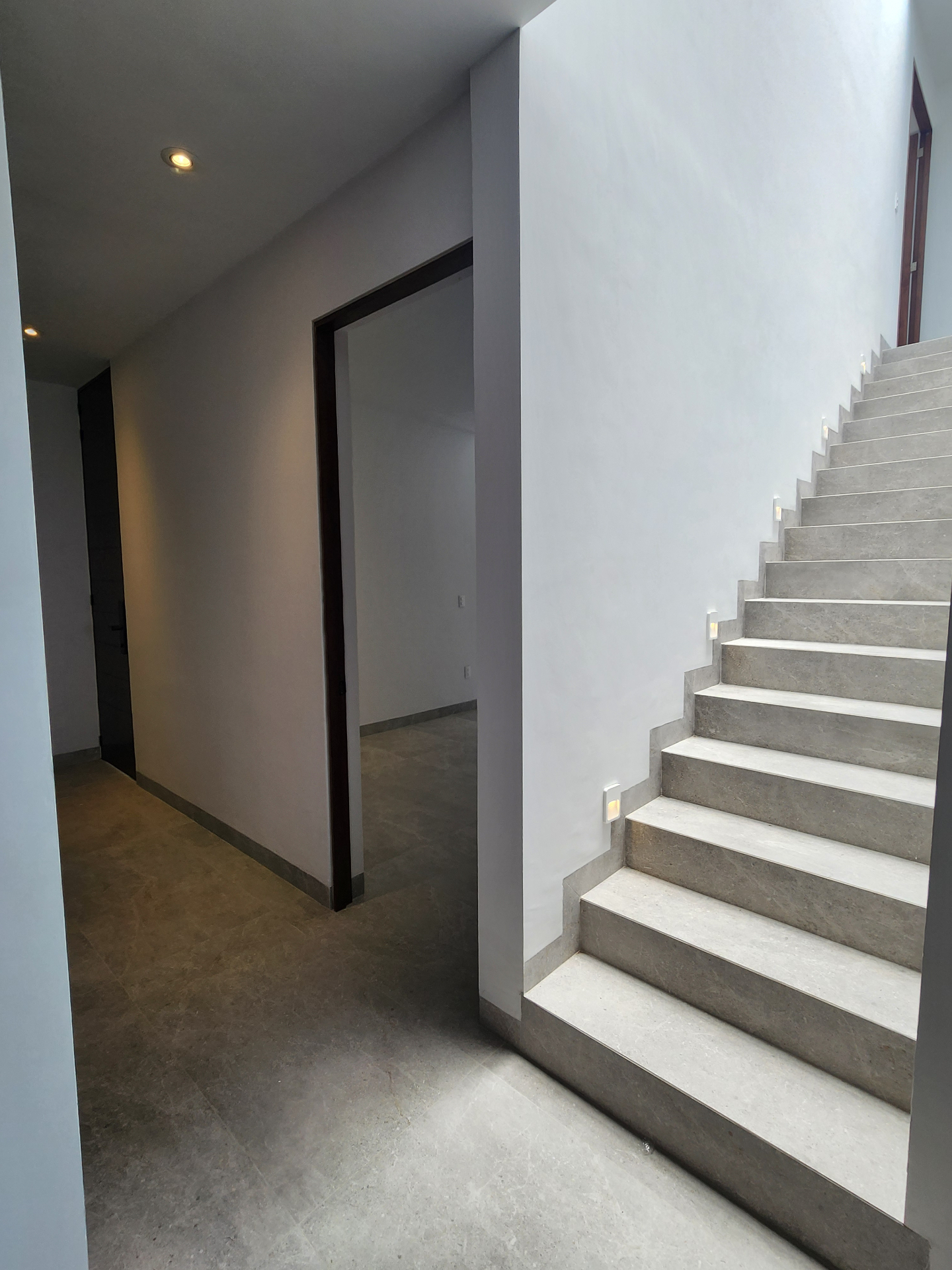 Vestíbulo interior con escalera revestida en piedra, iluminación de huella y circulación hacia recámara principal