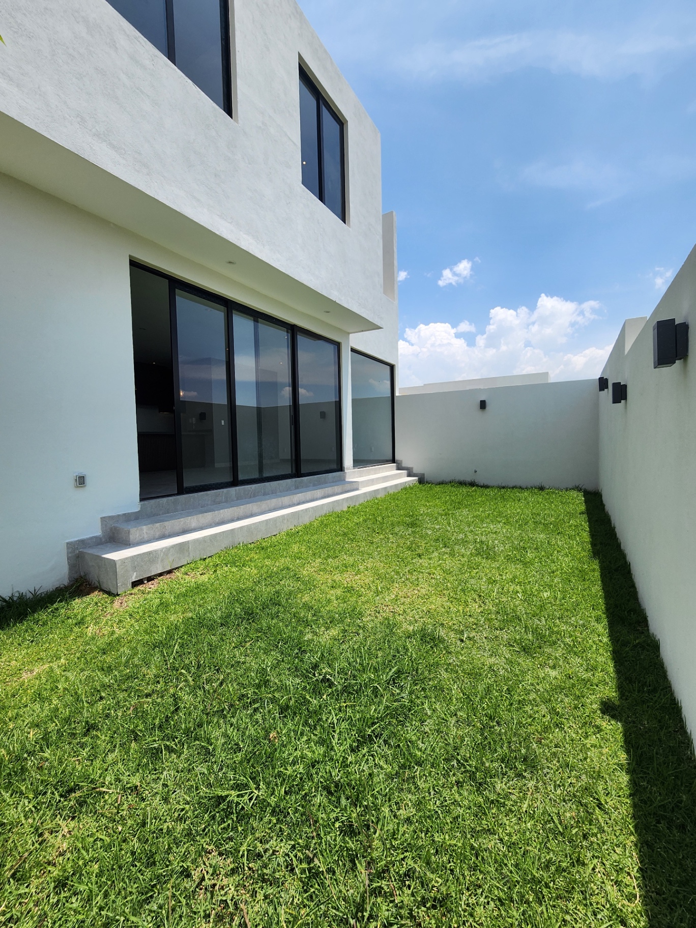 Jardín trasero con pasto natural, escalinatas de acceso y muro perimetral en blanco
