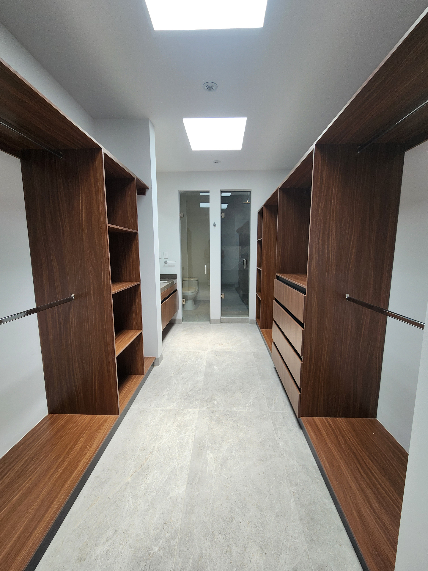 Vestidor doble con carpintería en madera, tragaluz cenital y acceso directo al baño principal
