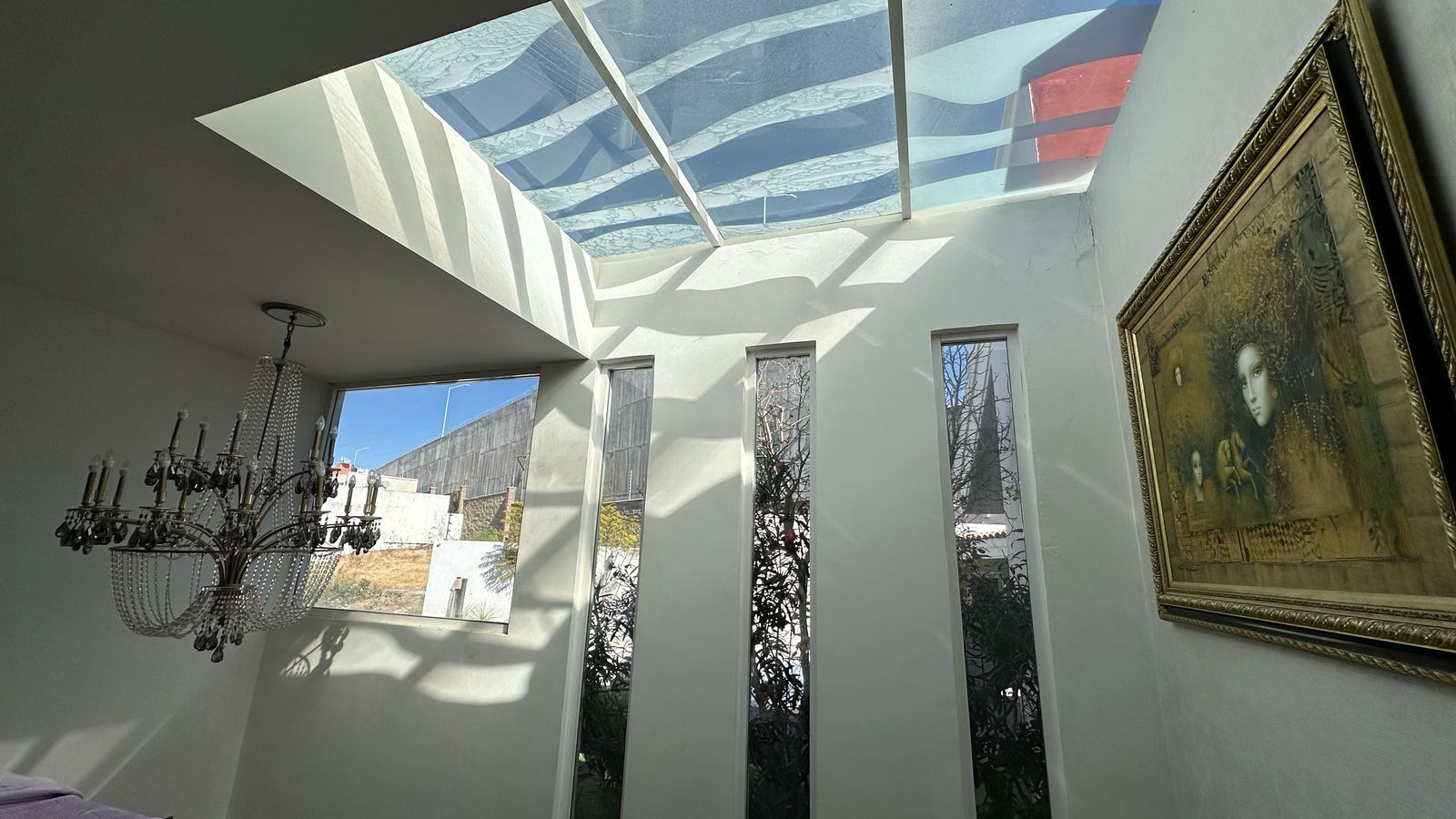 Tragaluz con doble altura, candelabro de cristal y muros blancos iluminados
