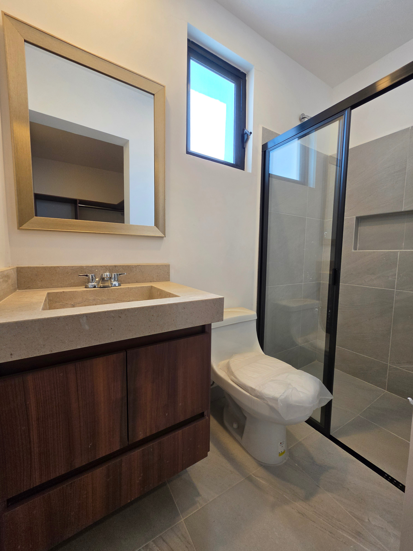 Baño completo con cancel de cristal templado, mueble de madera y lavabo en cubierta de piedra