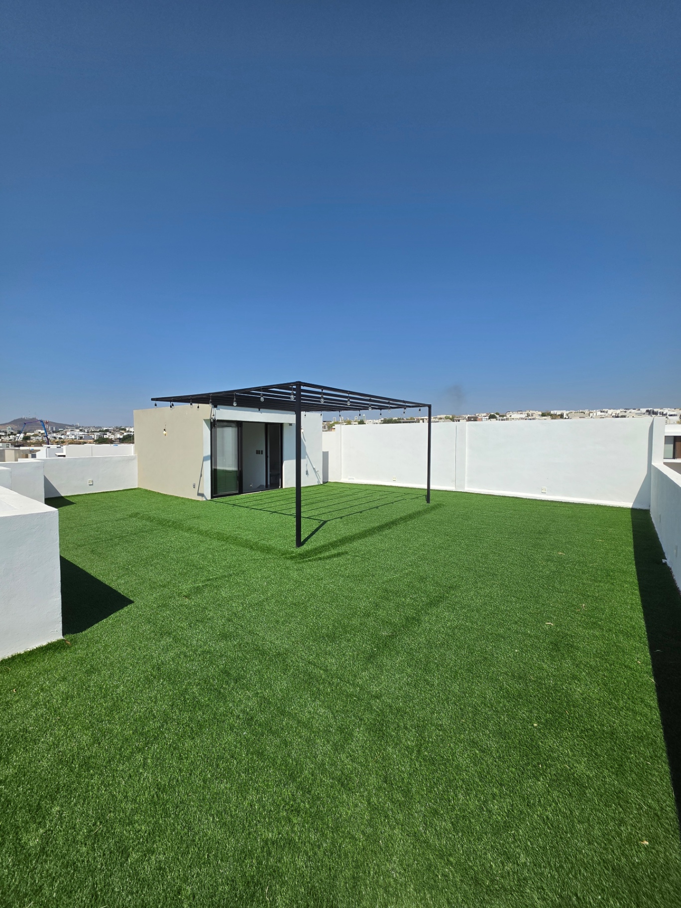 Roof top con pasto sintético, pérgola metálica con luces y muros perimetrales blancos