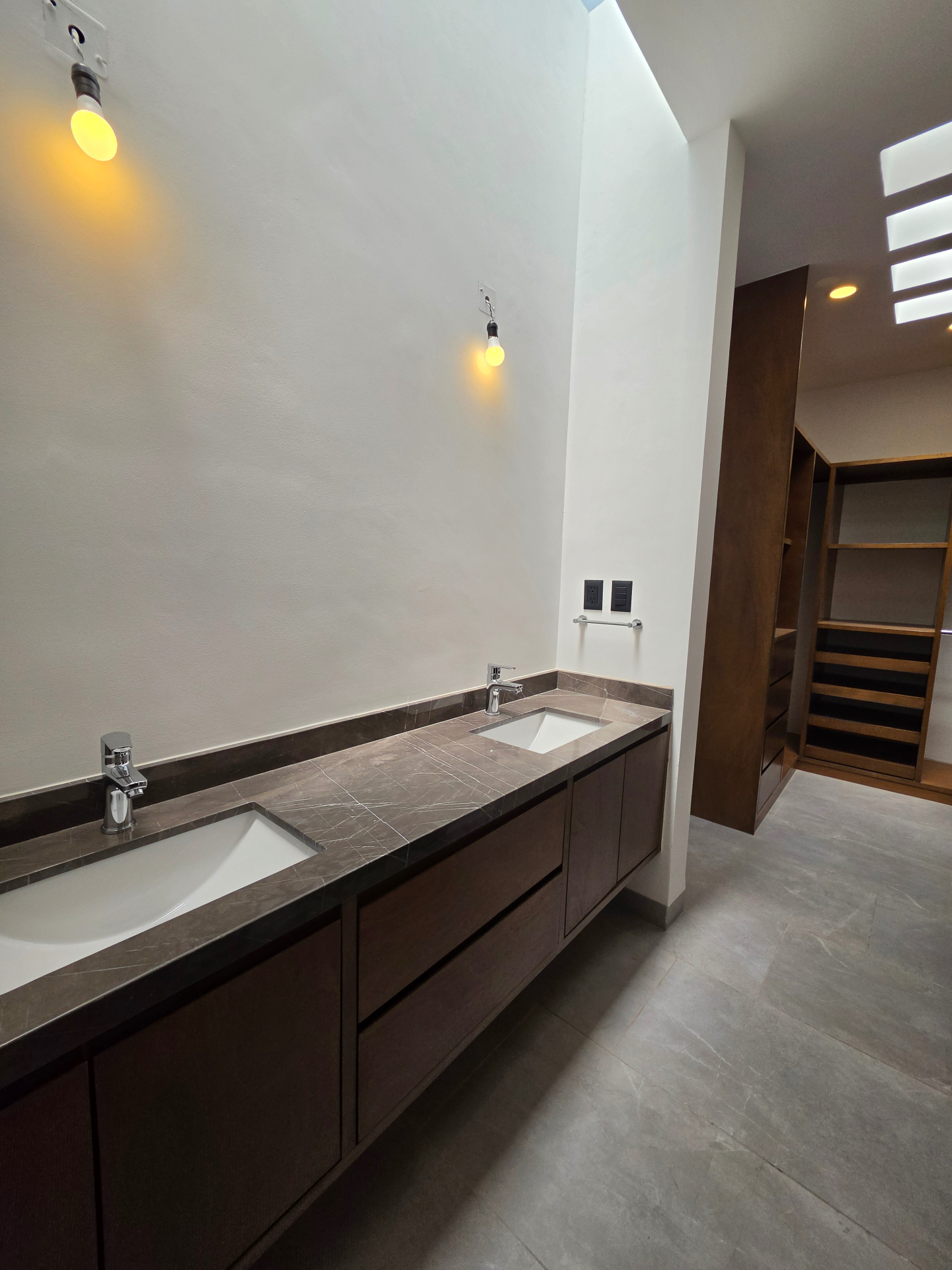 Baño principal con doble lavabo, cubierta de mármol gris y mobiliario en madera oscura