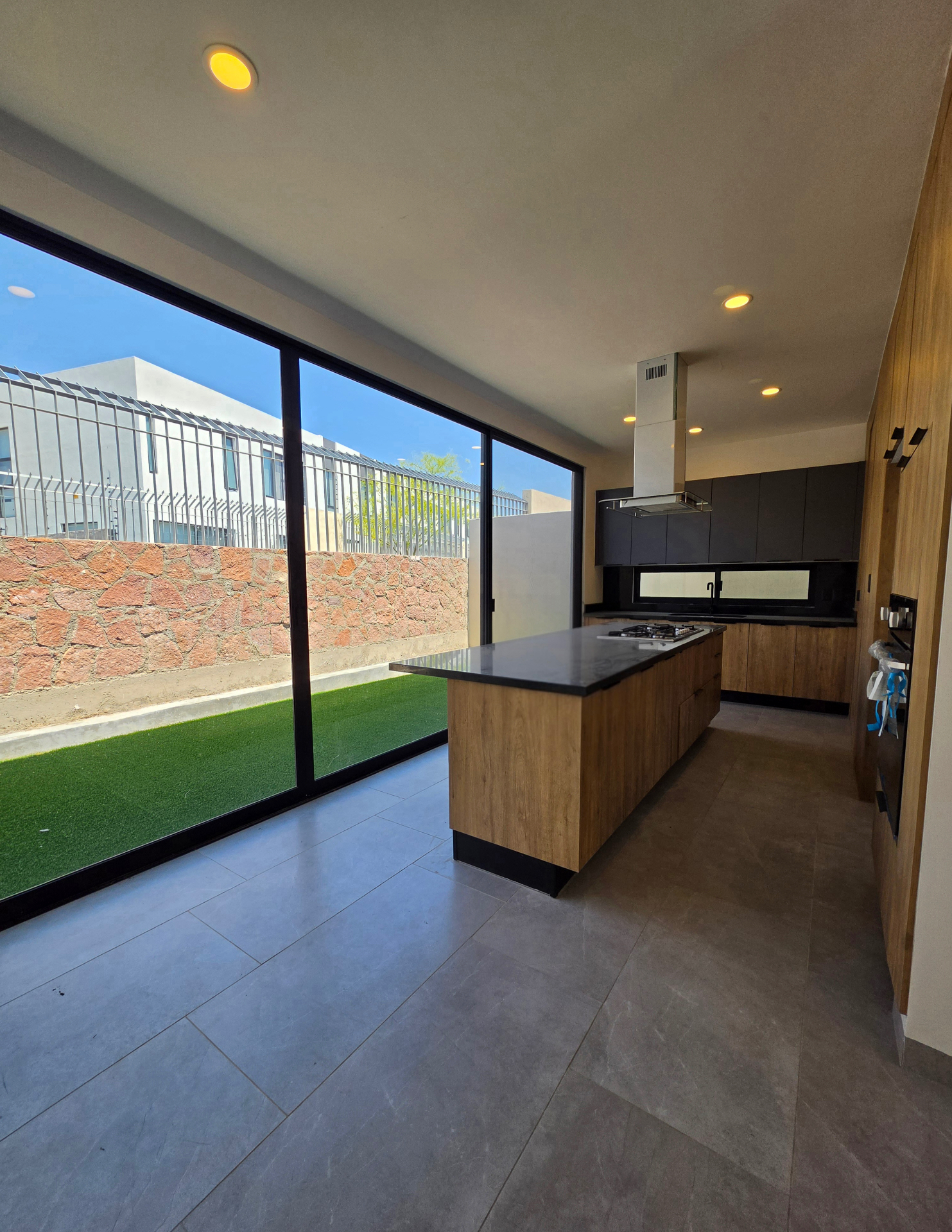 Cocina lineal con isla, ventanal completo al jardín lateral y acabados en madera y negro mate